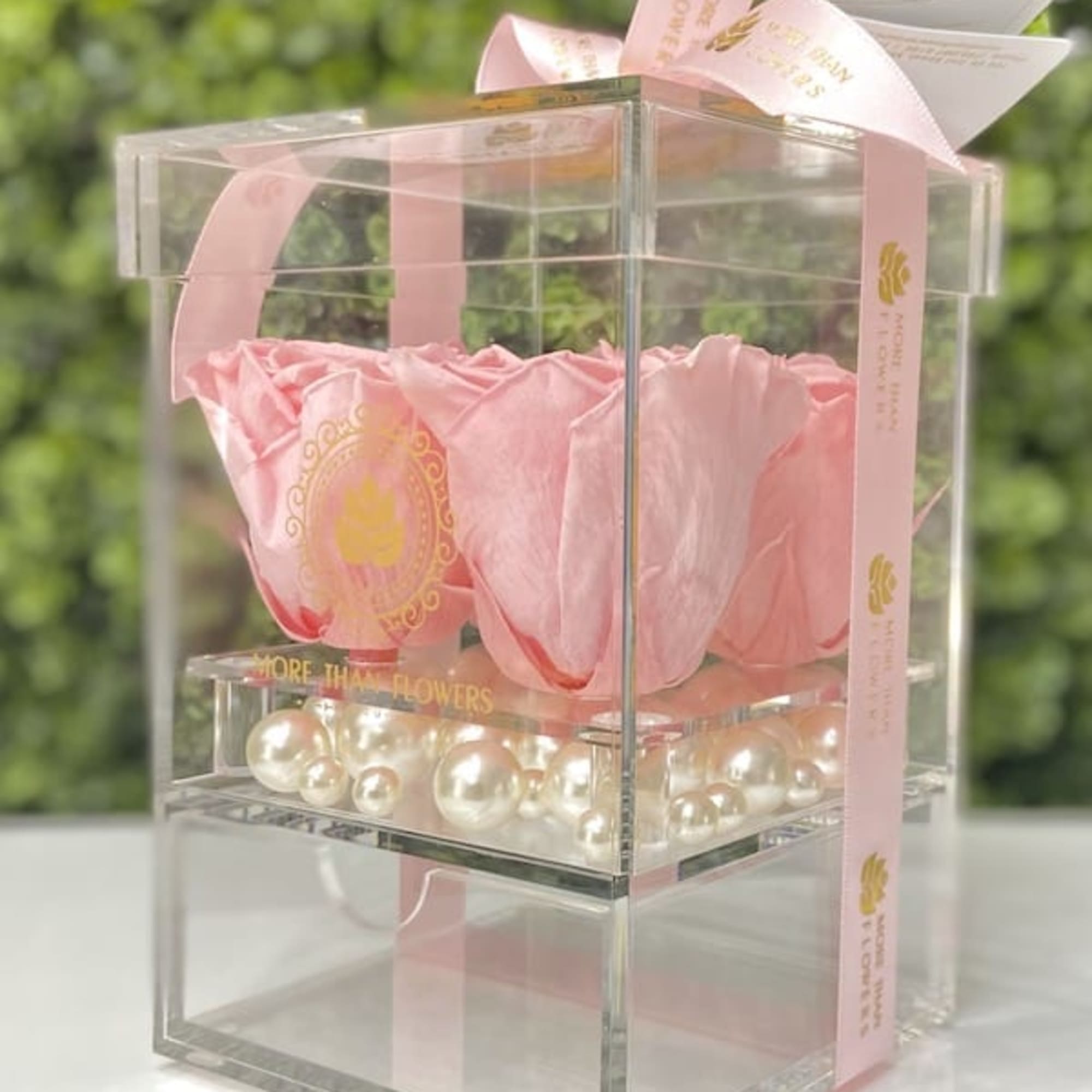 Pink roses in a clear acrylic box with pearl accents and a pink ribbon
