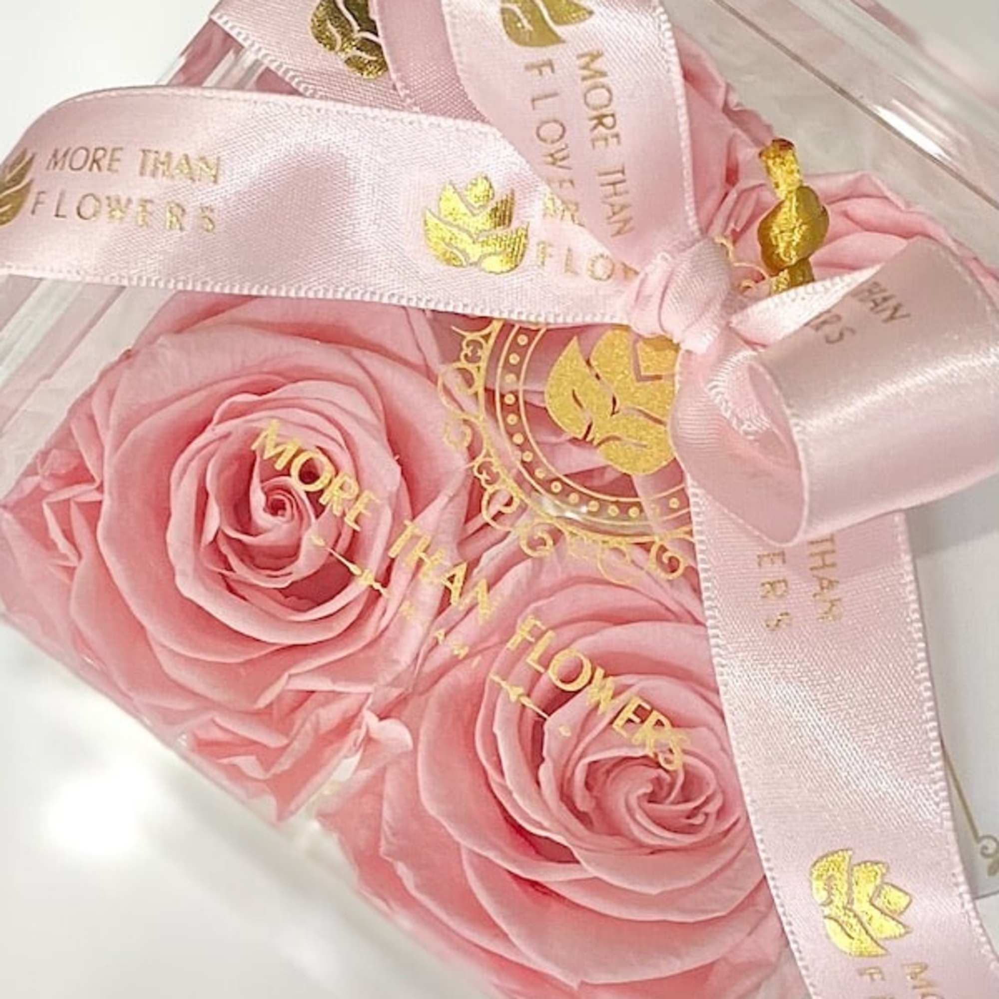Acrylic box with pink roses topped with a pink satin ribbon printed with gold text