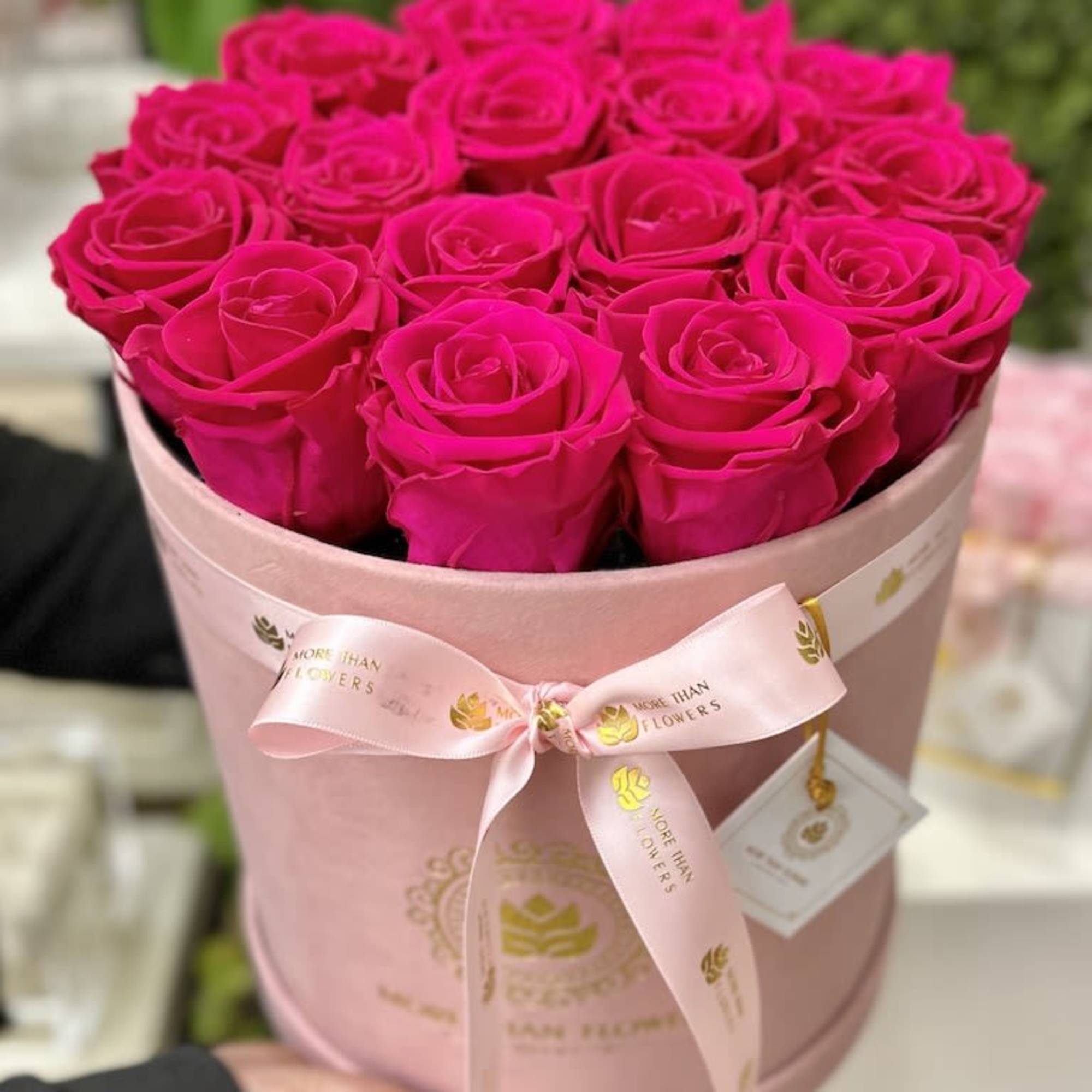 Round pink box filled with tightly packed hot pink roses and tied with a satin ribbon.