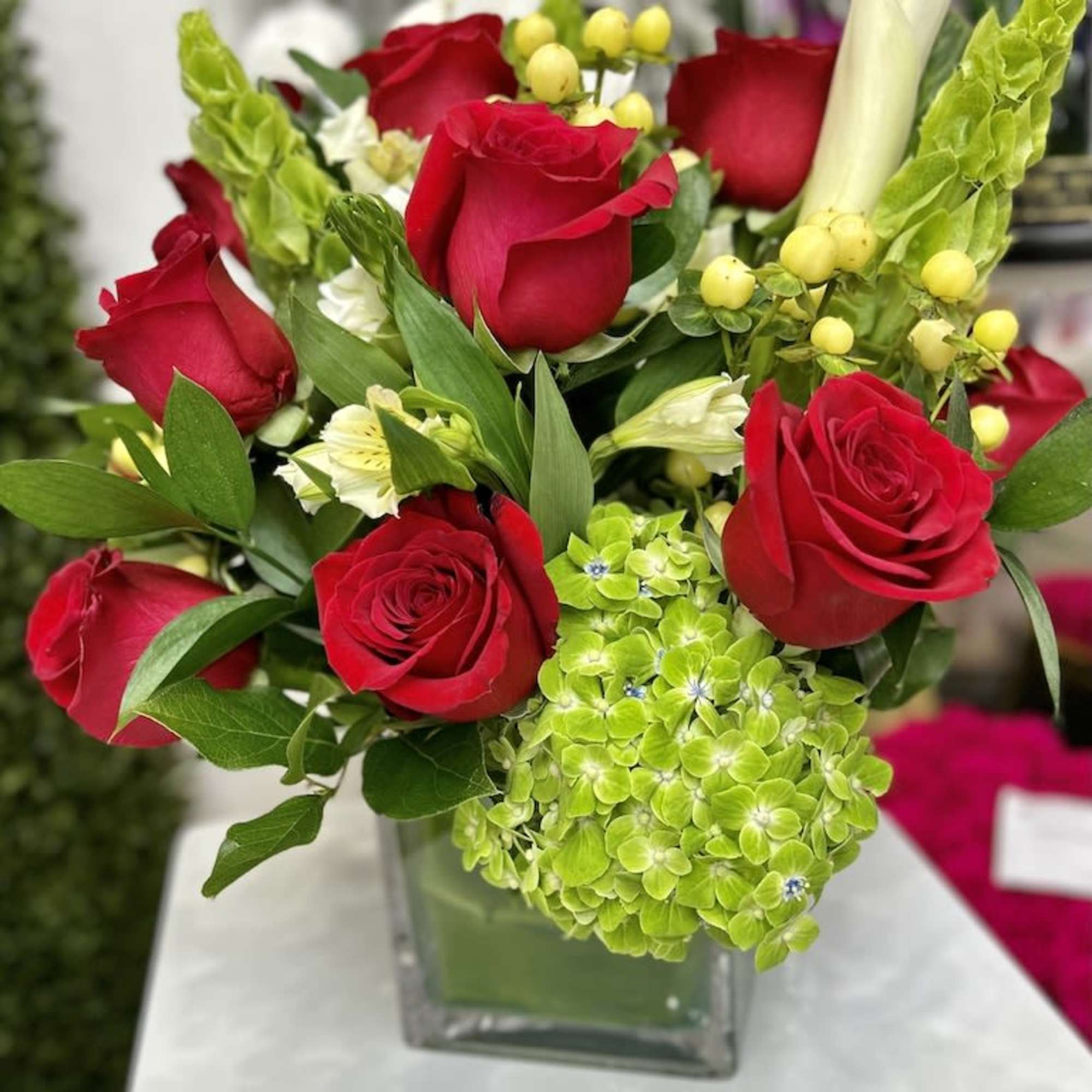Red roses with green hydrangea and white calla lily in a clear glass cube vase