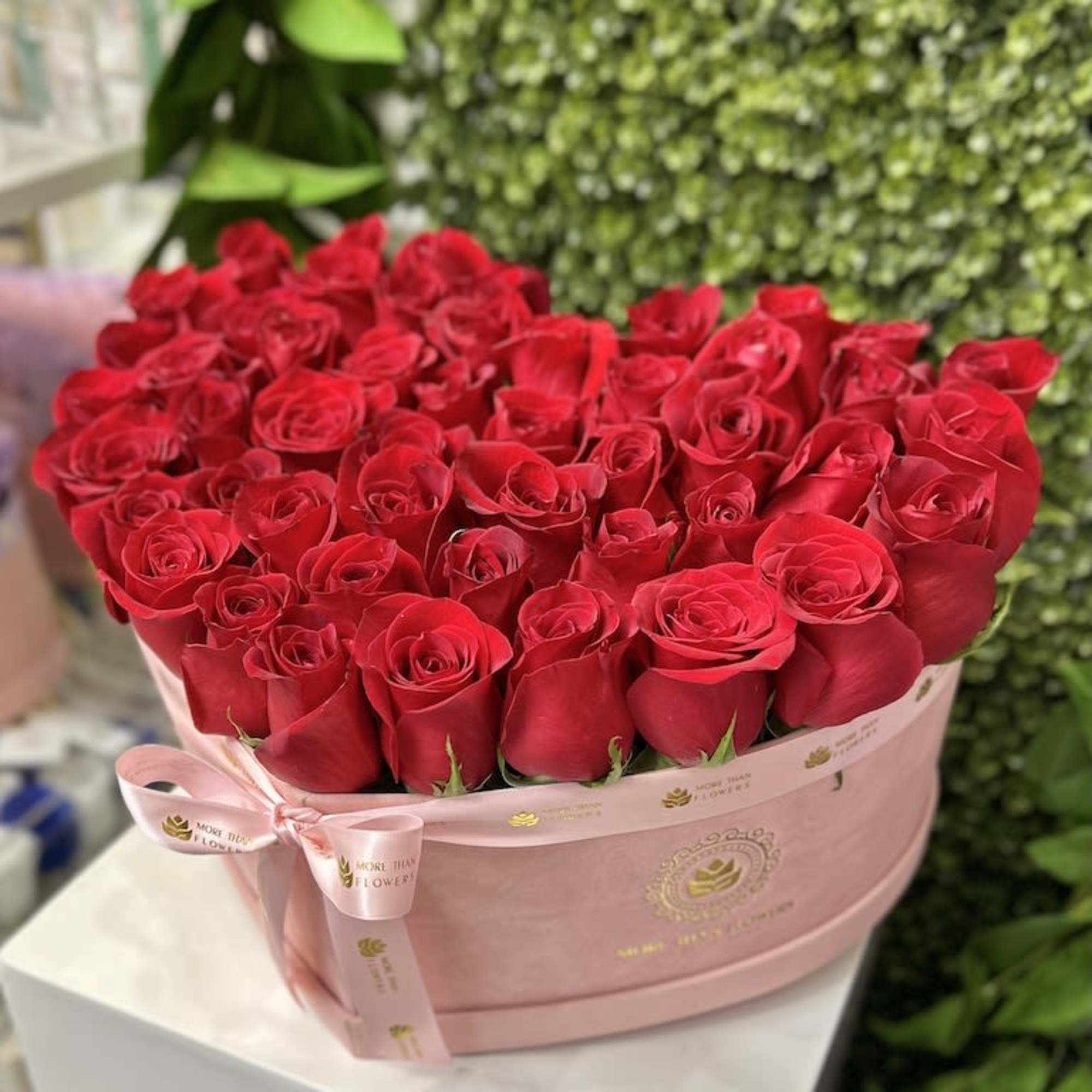 Heart-shaped pink hatbox filled with tightly packed red roses and tied with a pink ribbon