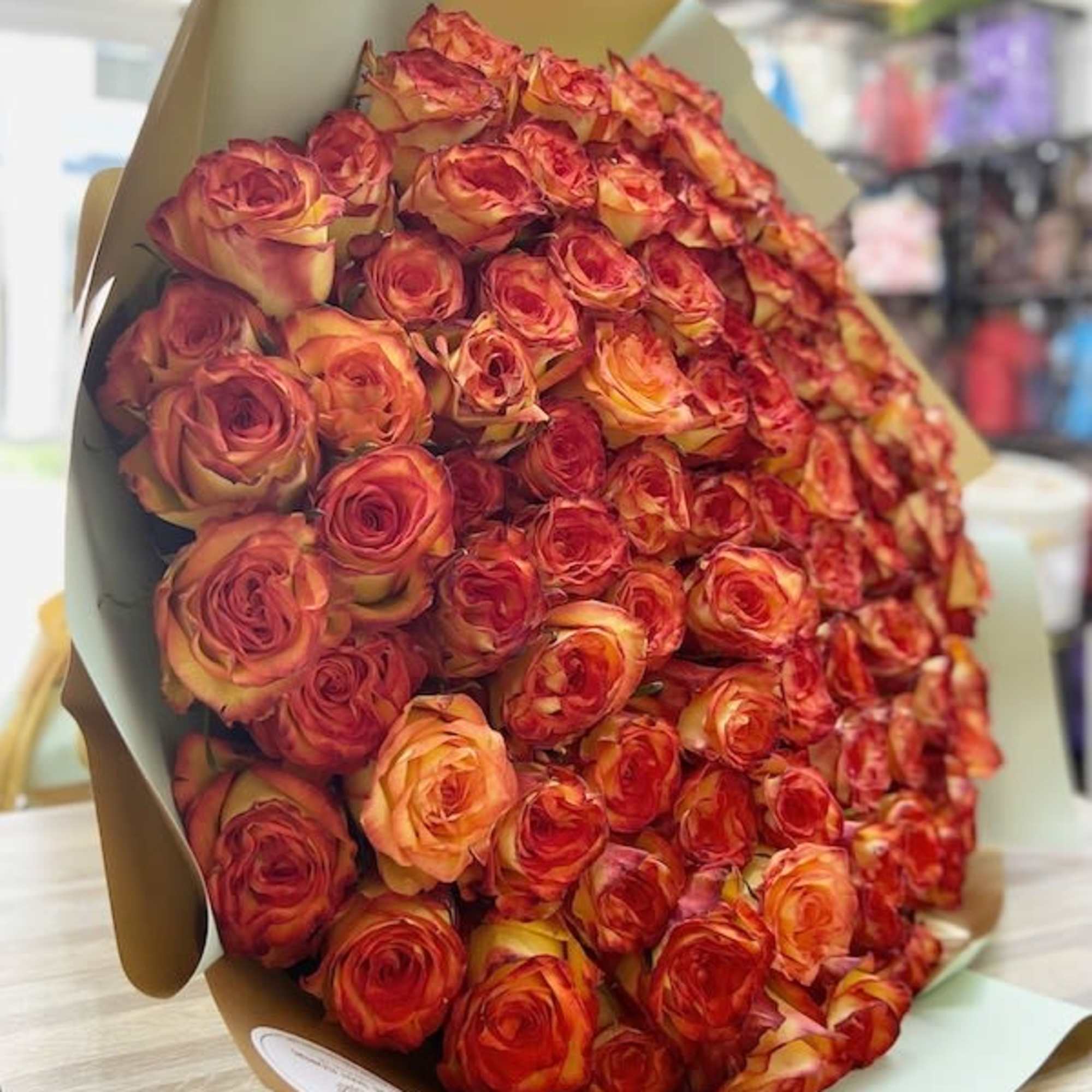 Oversized bouquet of orange and red roses wrapped in tan and pale green paper on a table