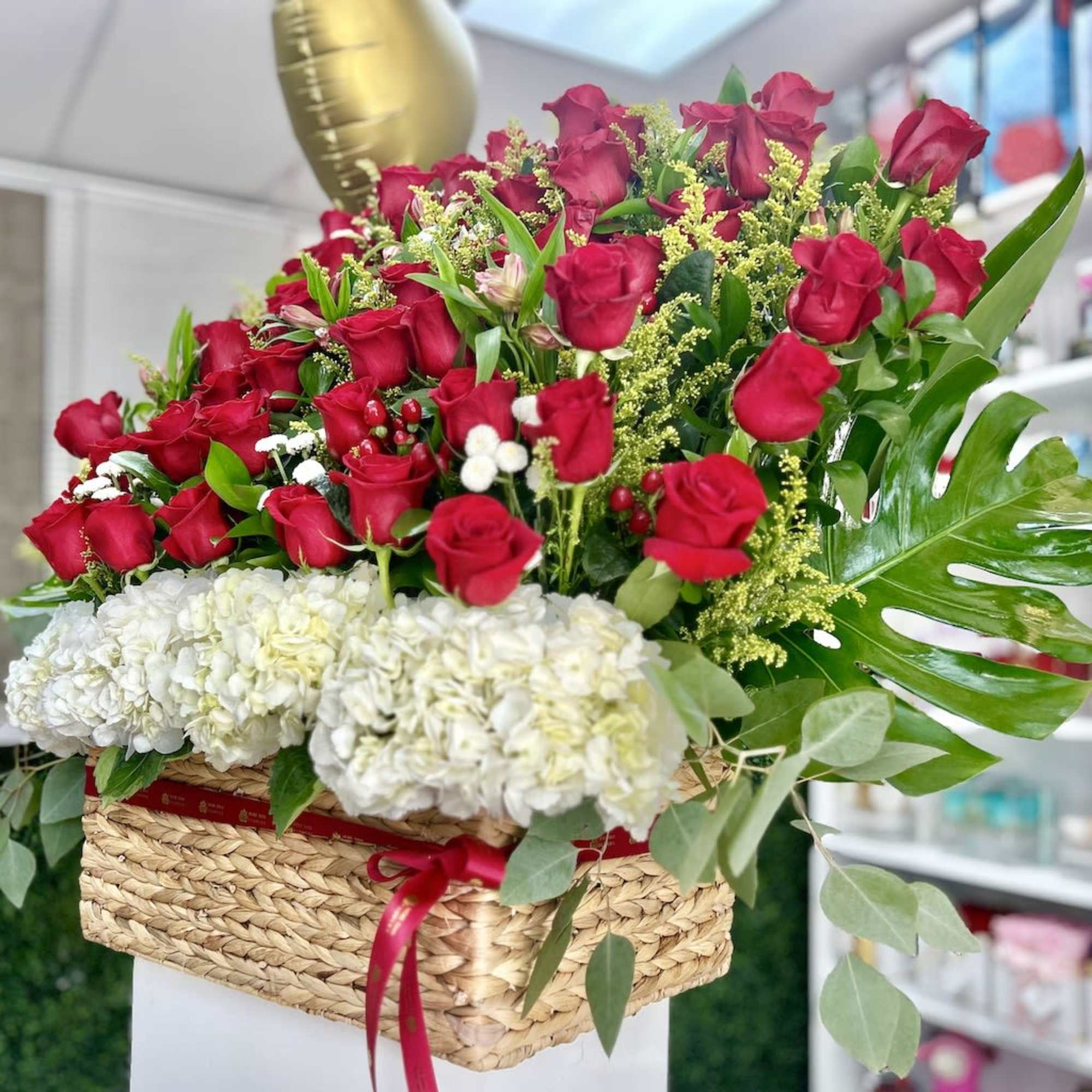 Large basket arrangement of red roses and white hydrangeas with a gold balloon.