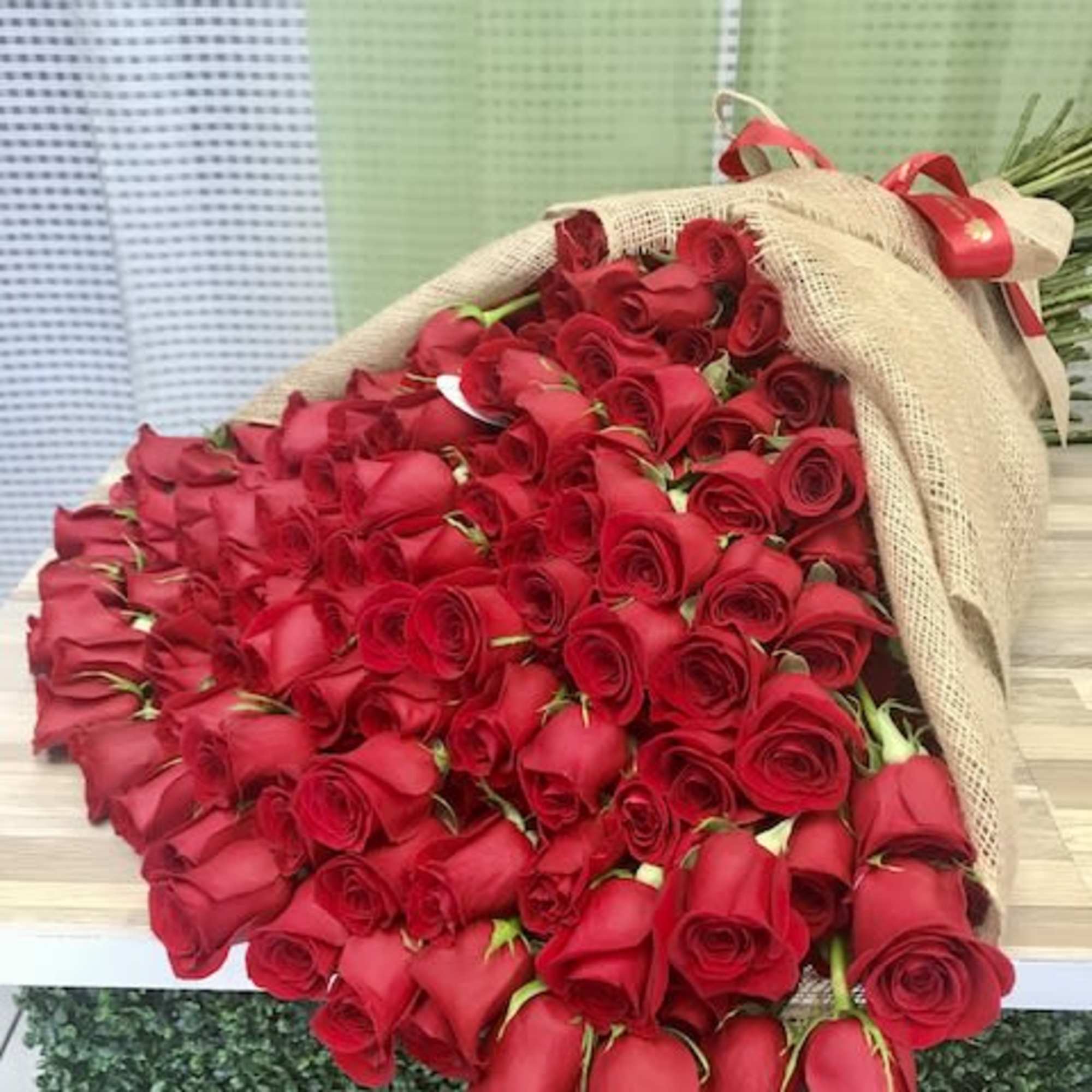 Large bouquet of many red roses wrapped in burlap with a red ribbon bow.
