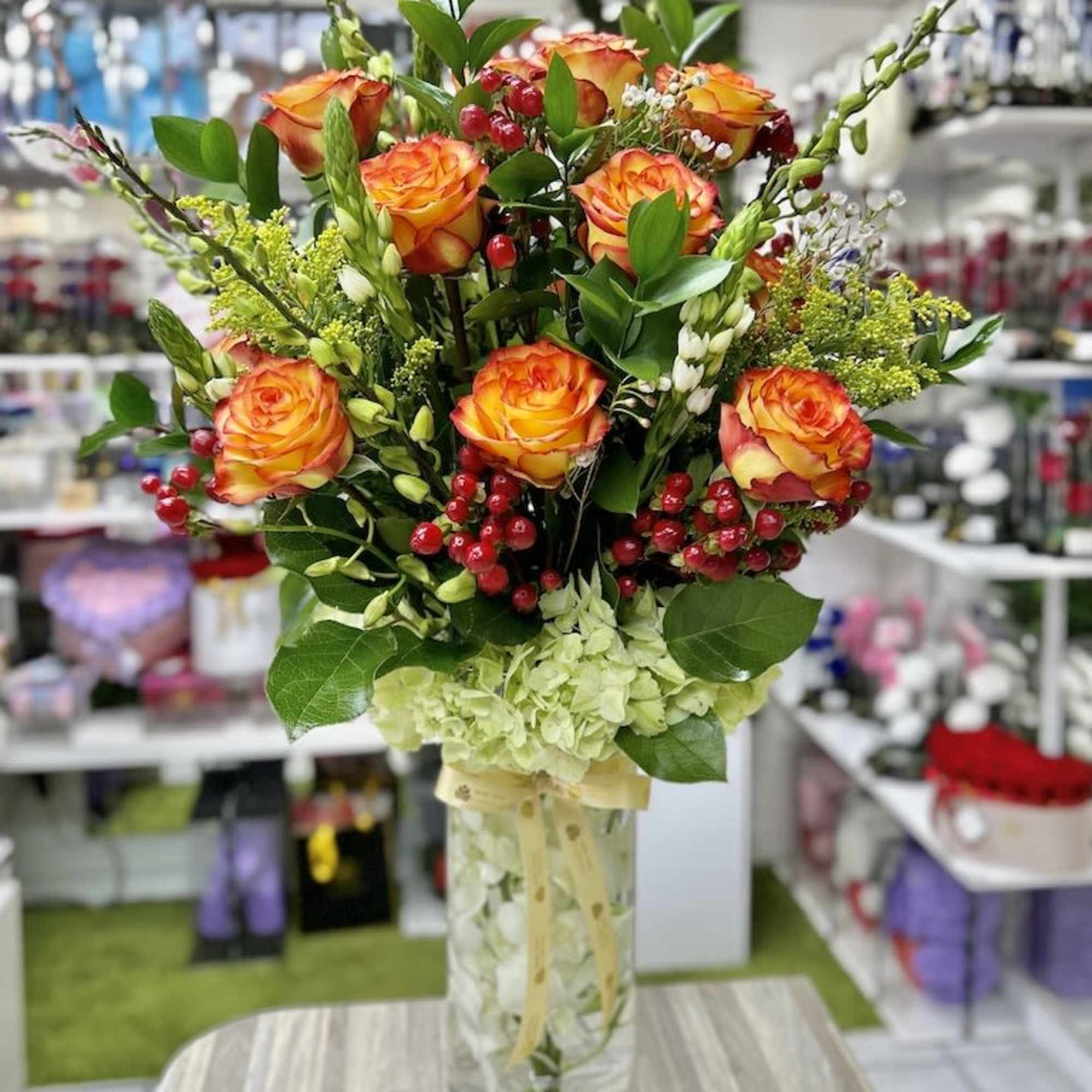 Tall glass vase of orange roses, green hydrangea, and red berries in a mixed floral arrangement