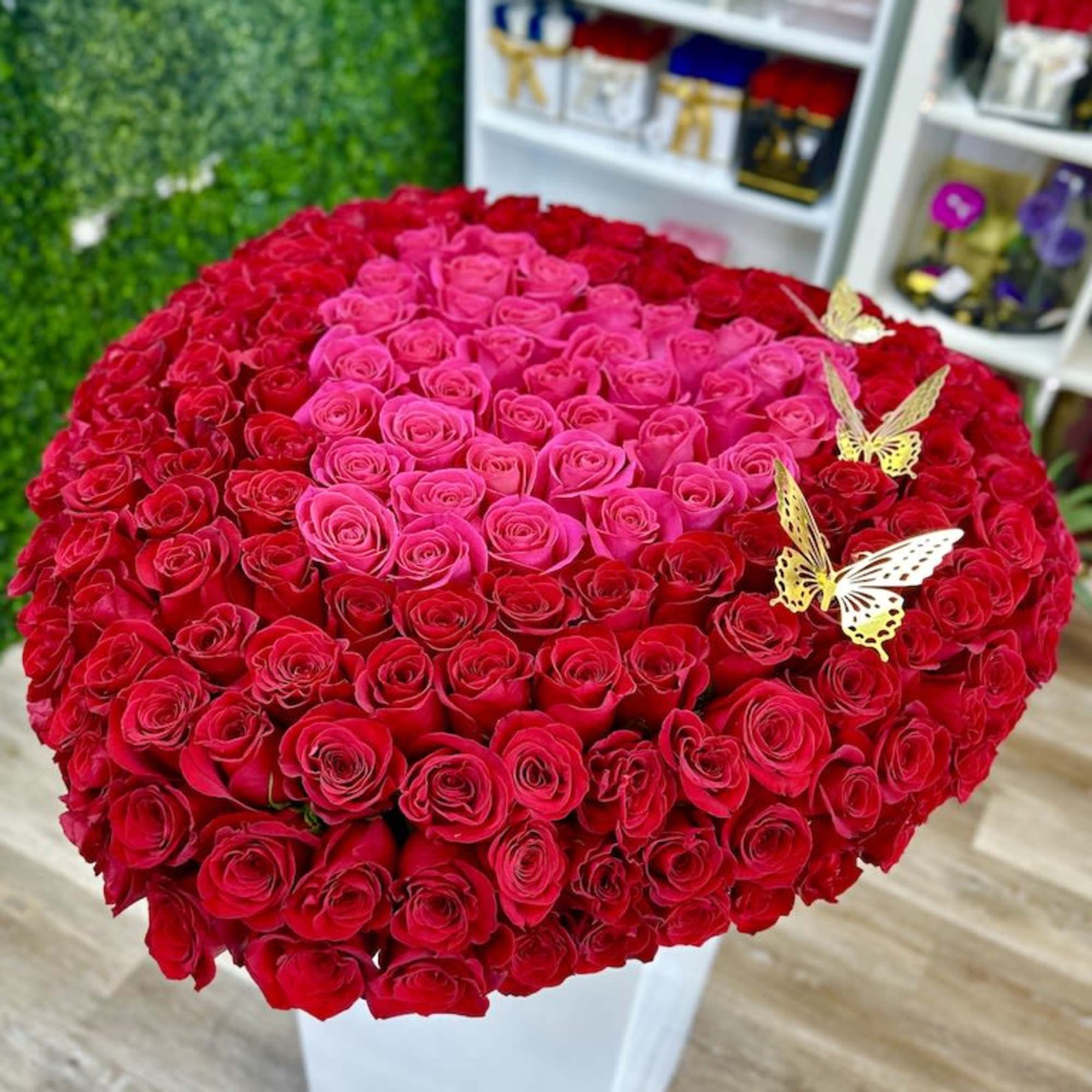 Large heart-shaped arrangement of red and hot pink roses on a white box with gold butterflies.