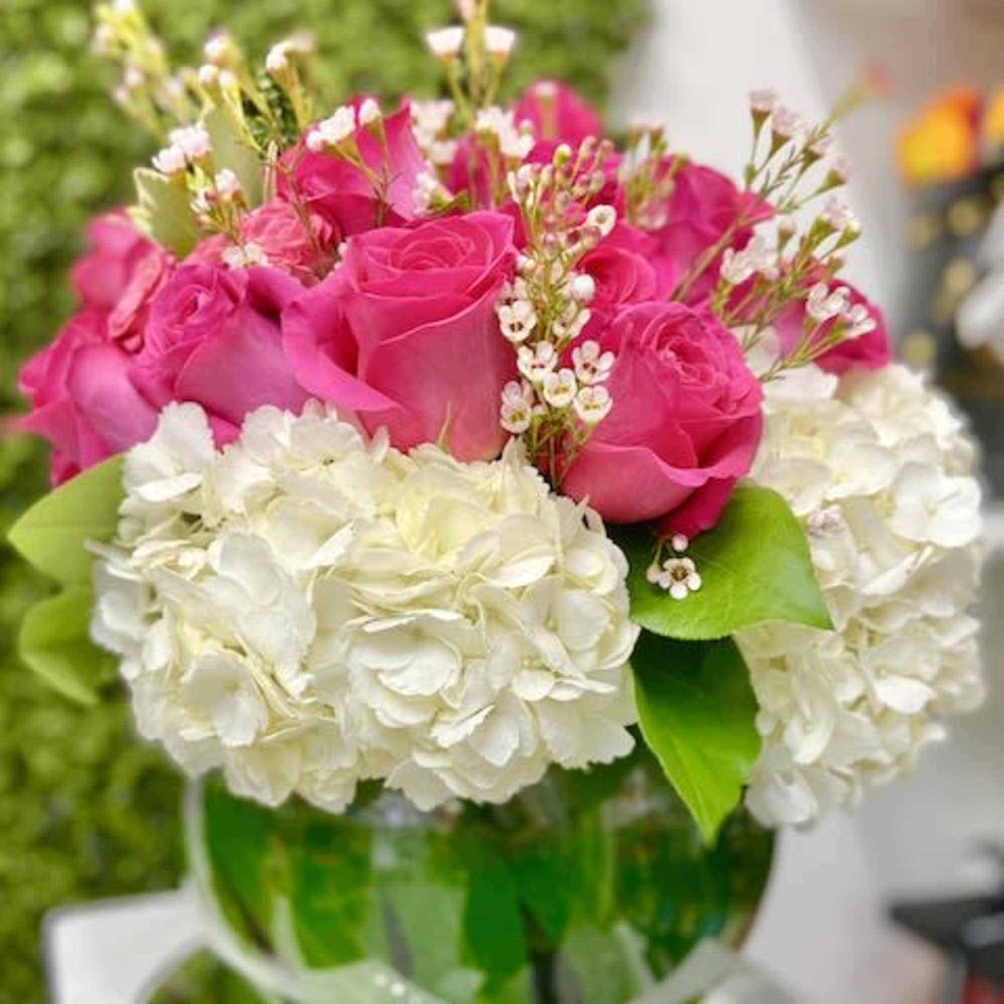Low round arrangement of hot pink roses and white hydrangeas in a green-accented glass bowl vase