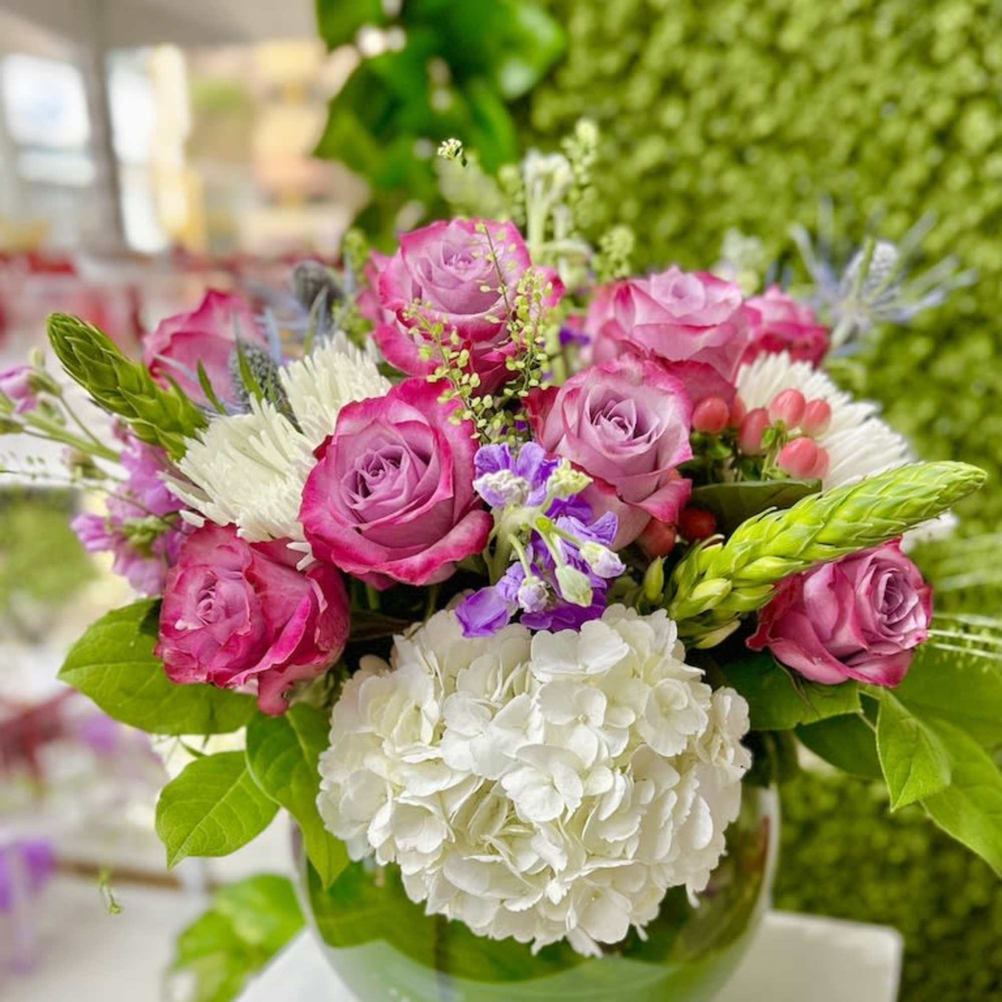 Round bouquet of pink roses, white hydrangea, and mixed blooms in a green glass vase