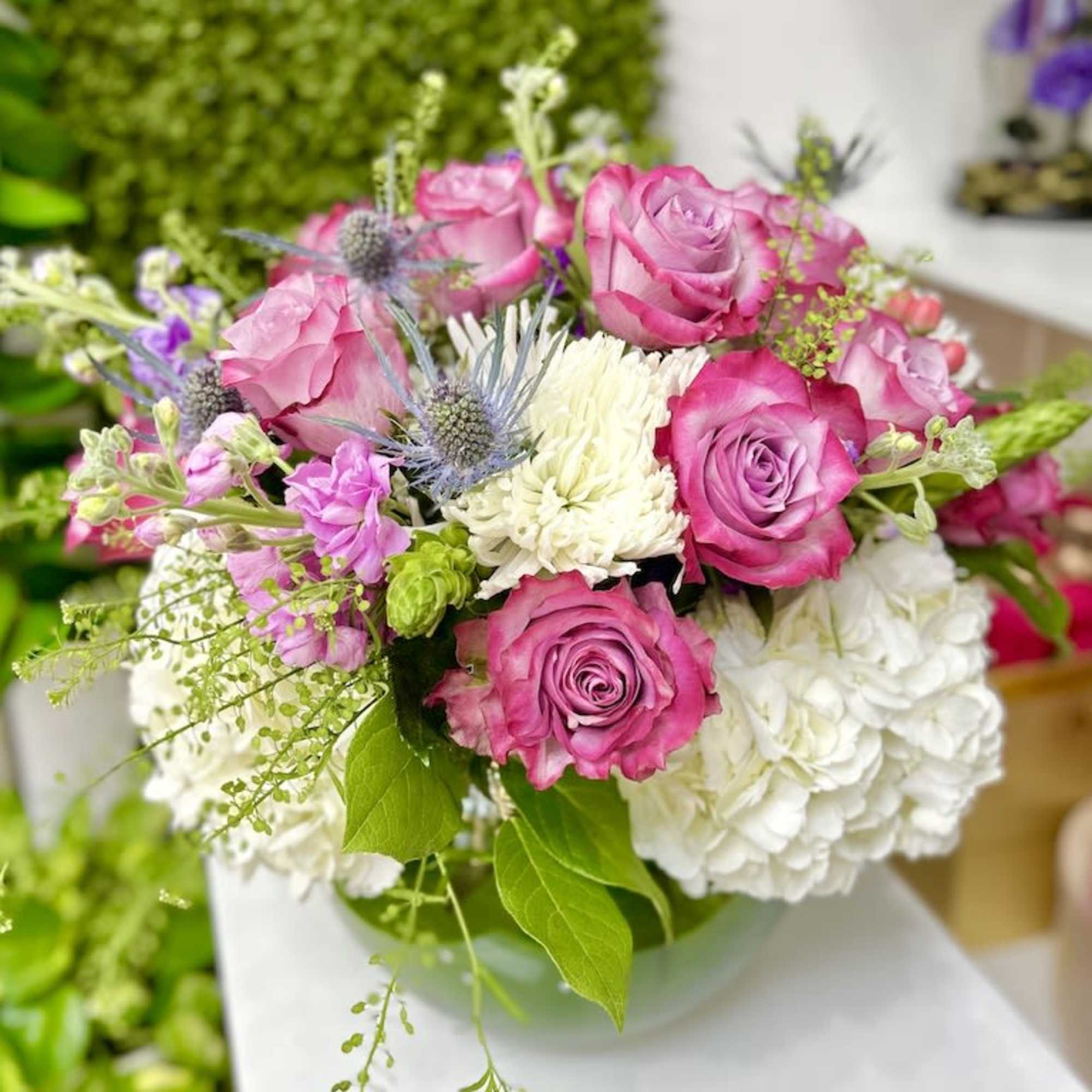 Low arrangement of pink roses, white hydrangeas, and mixed flowers in a round glass vase