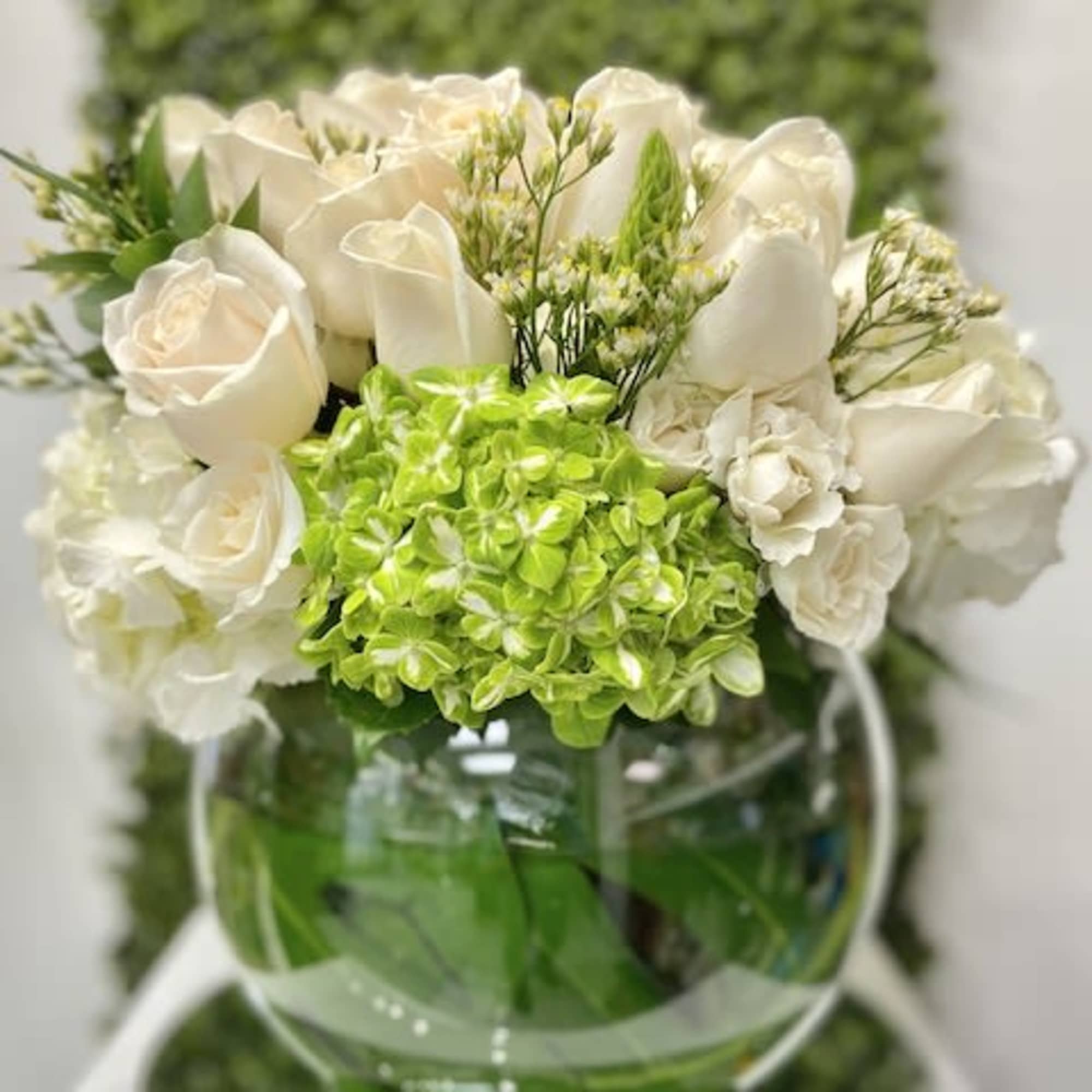 Low arrangement of white roses and green hydrangea in a round glass bowl vase