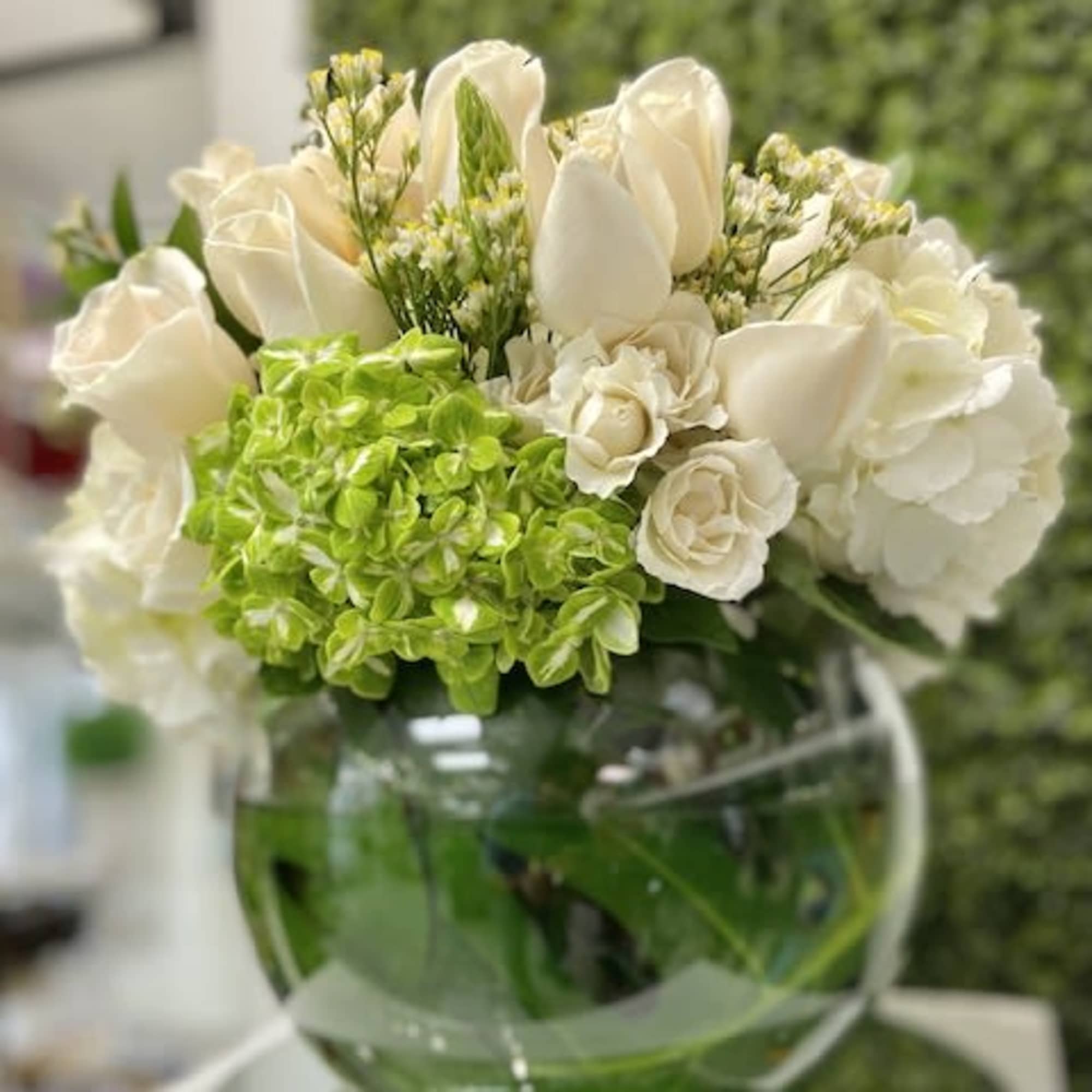 Low round arrangement of white roses and hydrangeas with green hydrangeas in a glass bowl vase