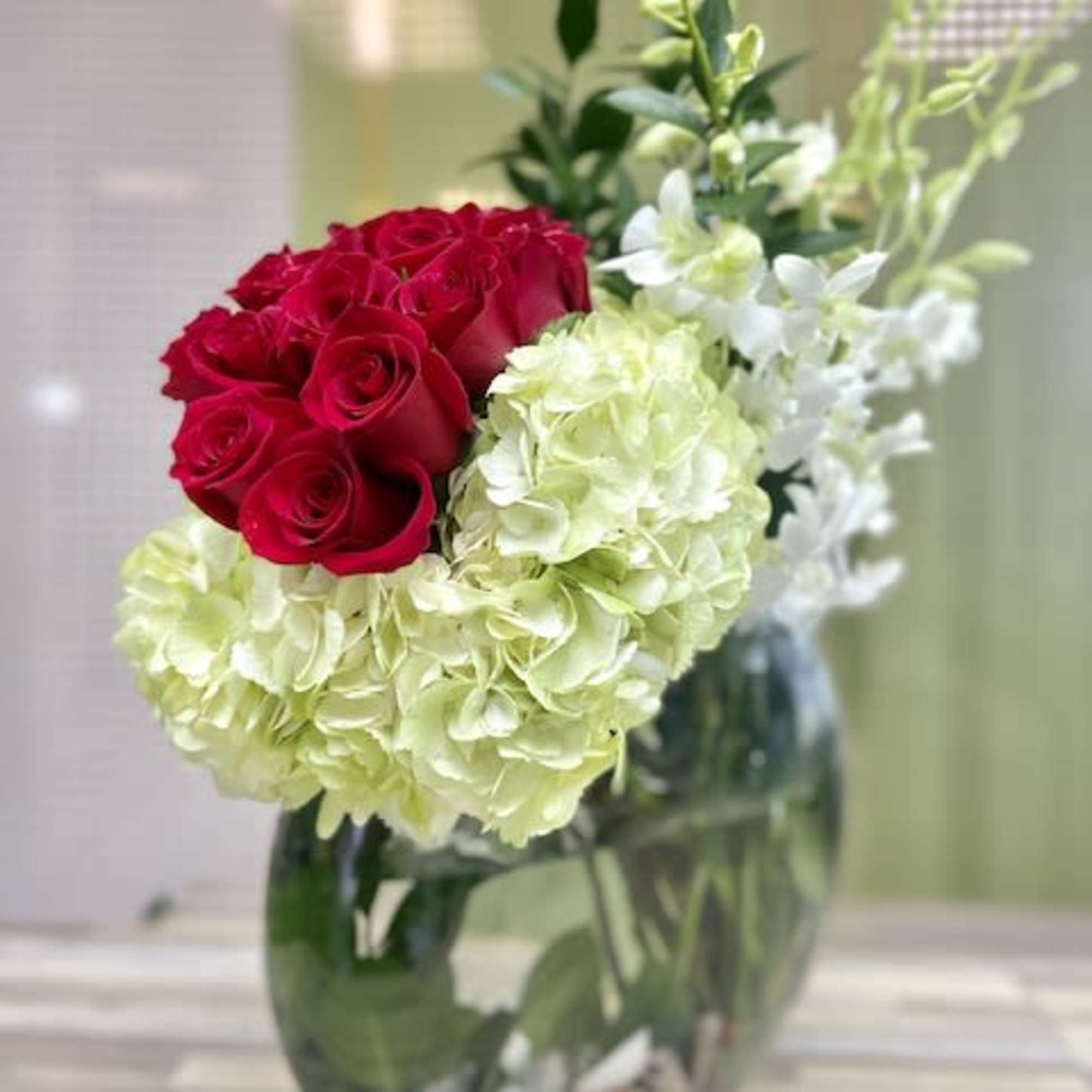 Asymmetrical arrangement of red roses, green hydrangeas, and white orchids in a clear glass vase.