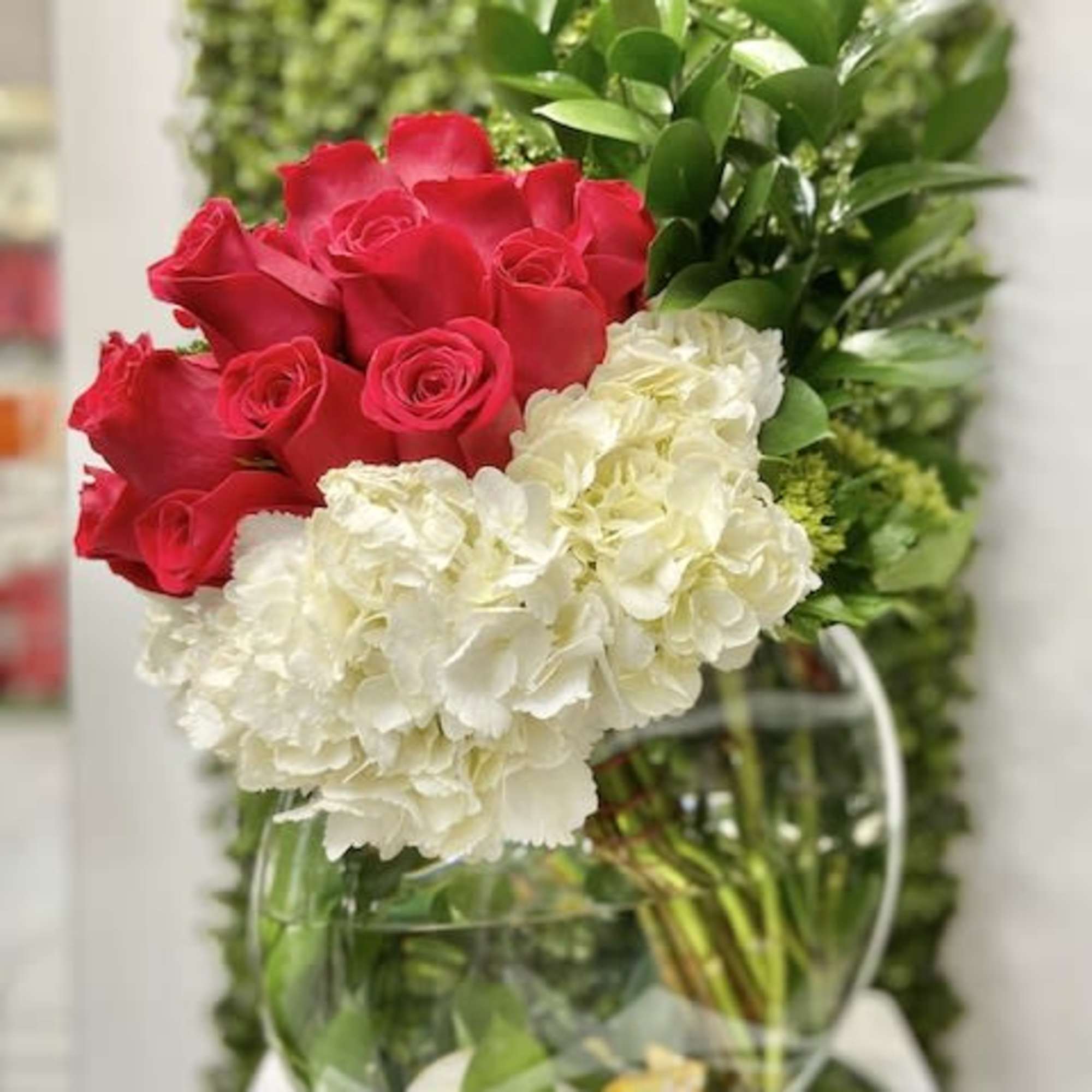 Modern arrangement of red roses and white hydrangeas in a round glass vase