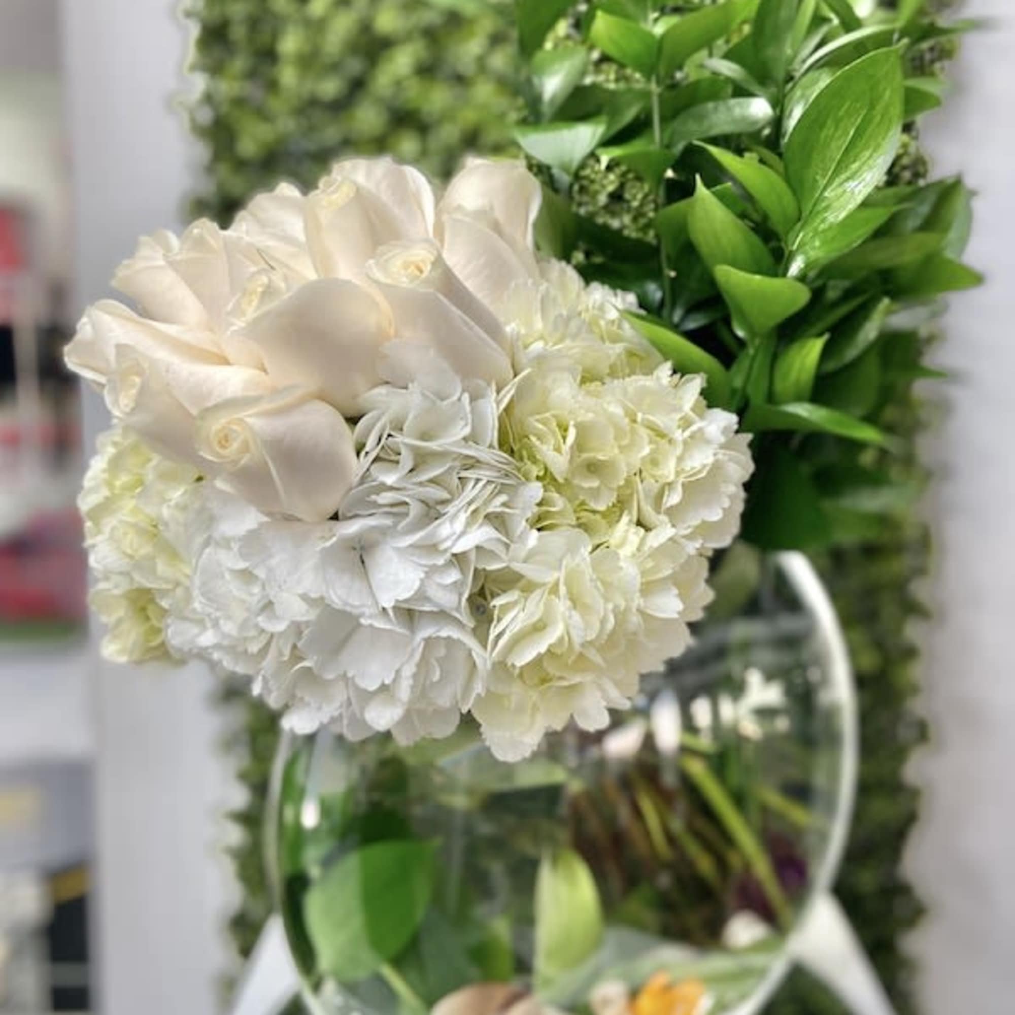 White roses and hydrangeas in a round glass vase with tall green foliage and submerged blooms.