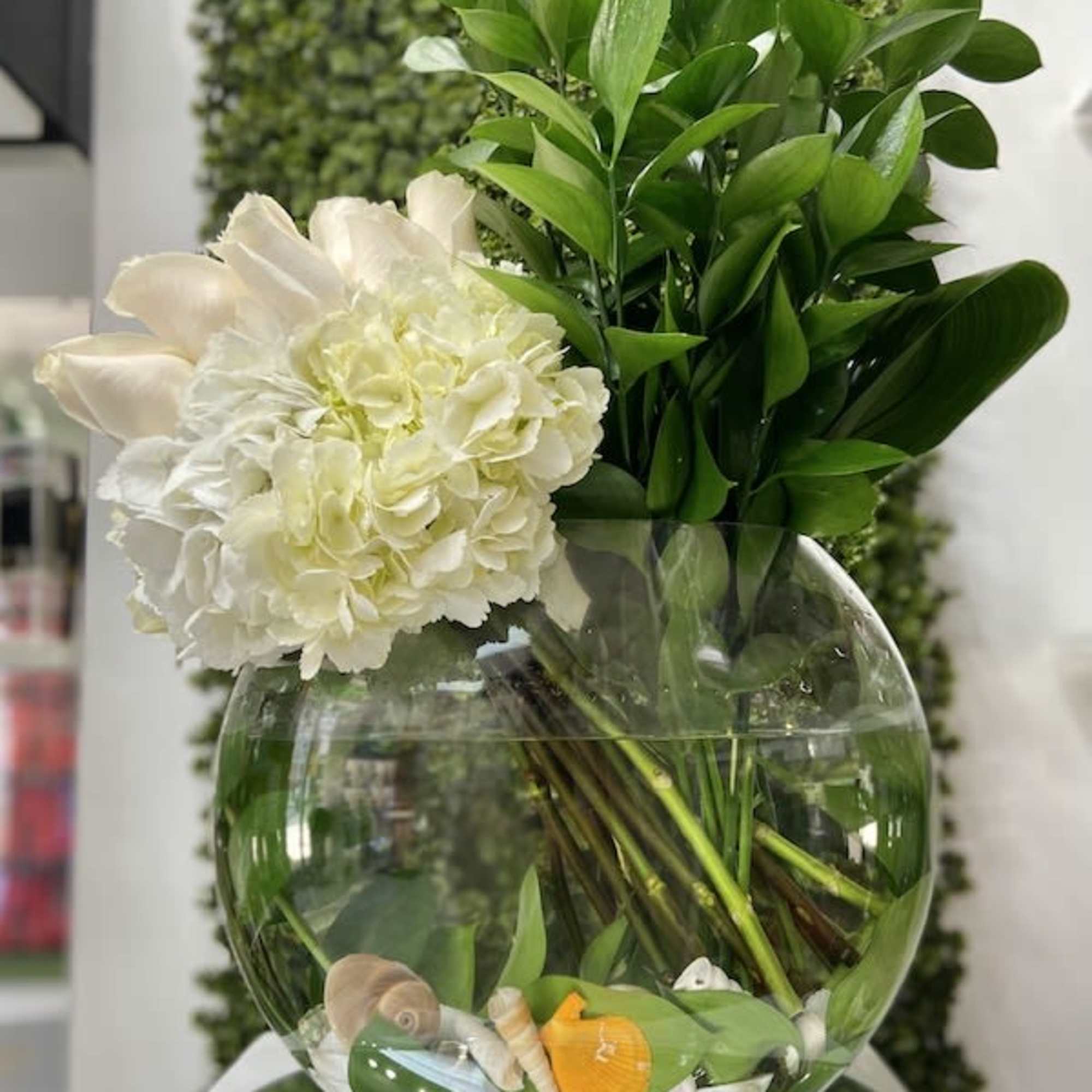 Round glass vase with white hydrangeas, pale calla lilies, and seashells submerged in water