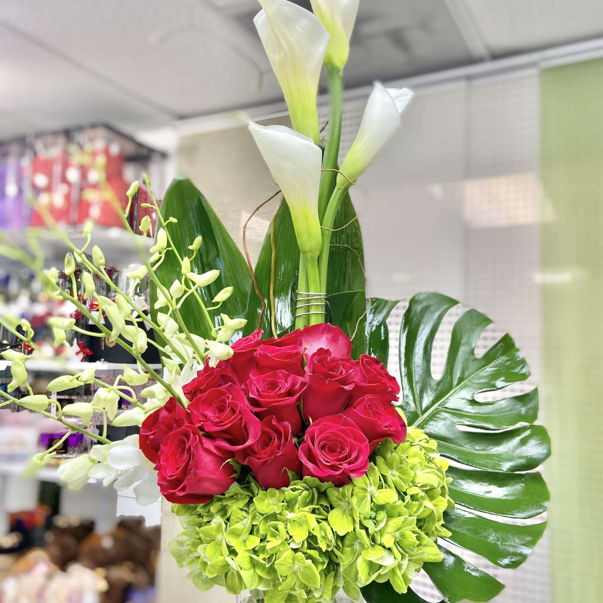 Tall arrangement with white calla lilies, red roses, green hydrangeas and orchids in a clear glass vase