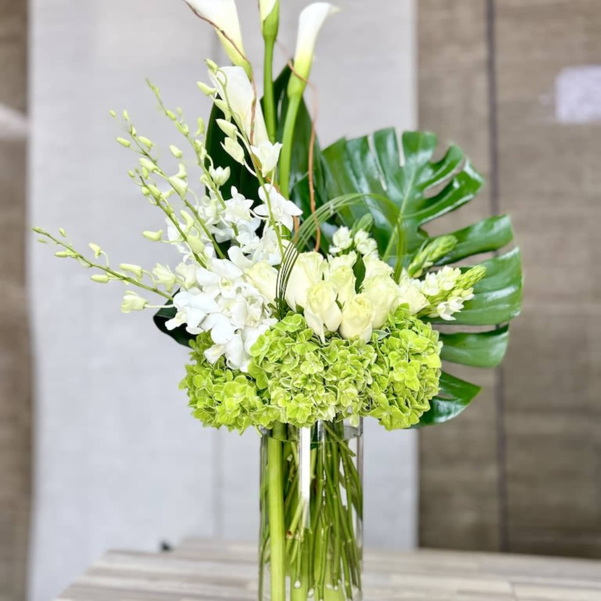 Tall white and green floral arrangement in a clear glass cylinder vase