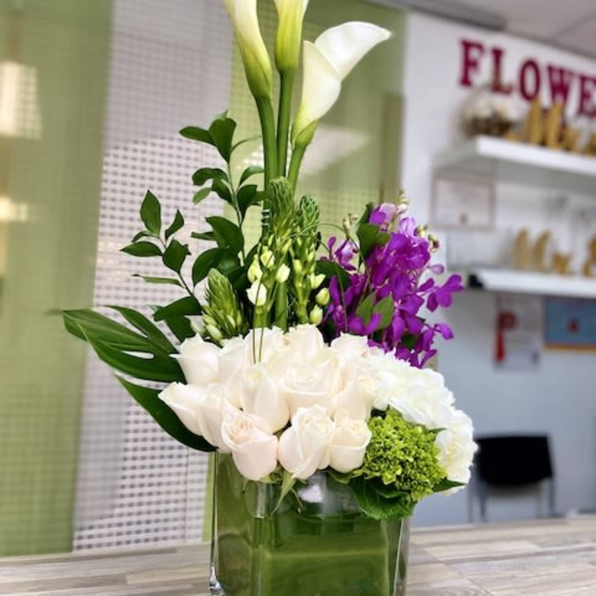 Tall modern arrangement with white calla lilies, white roses and purple orchids in a square glass vase