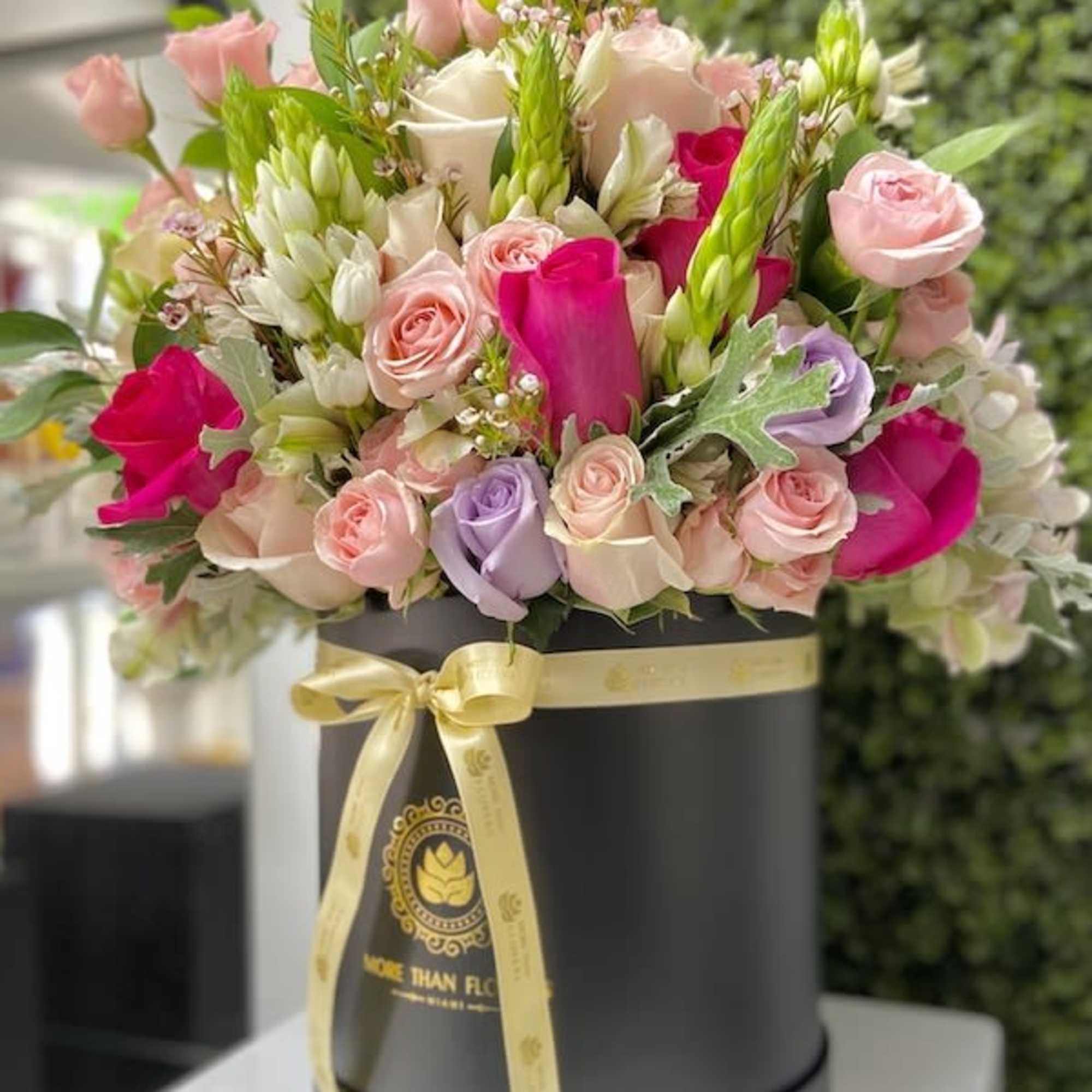 Pink, white, and lavender roses arranged in a black hatbox with a yellow ribbon bow