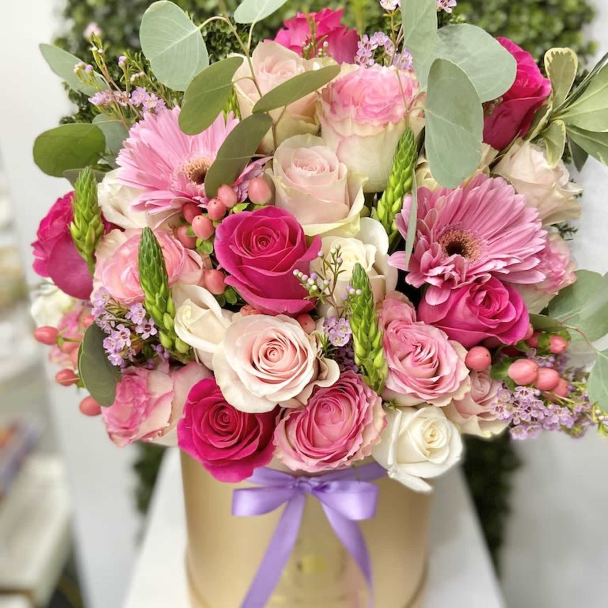 Pink and white rose arrangement with gerbera daisies in a round hatbox with purple ribbon