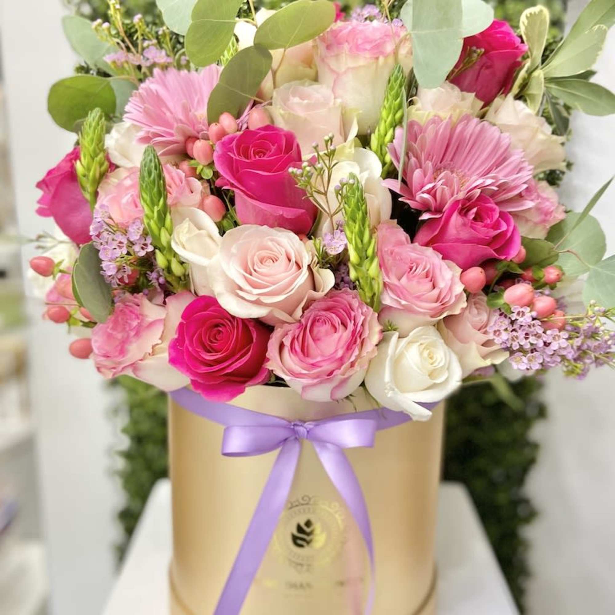 Pink and white roses with pink gerbera daisies arranged in a gold hatbox with a lavender ribbon