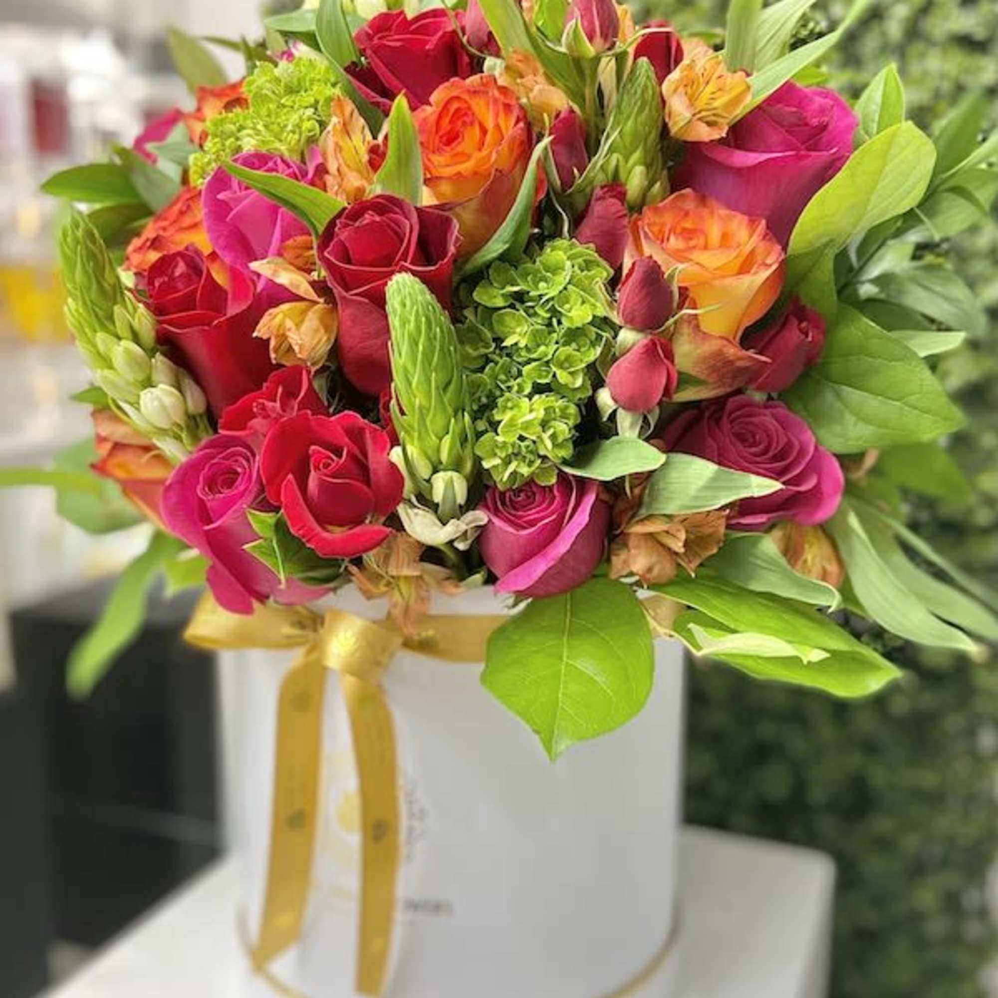 Bright bouquet of pink and orange roses in a white hat box with gold ribbon