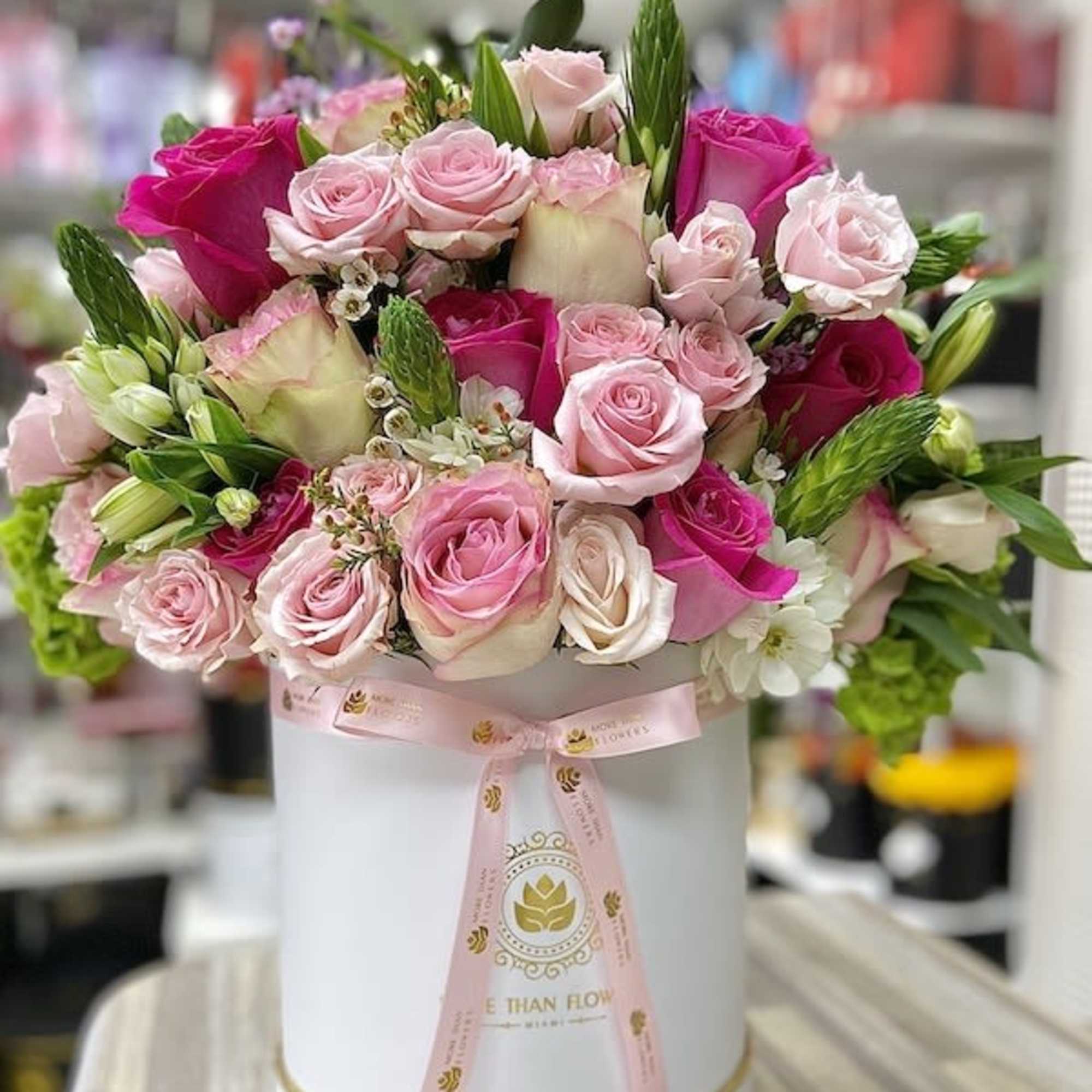 Round hatbox of pink and white roses with a pink ribbon on a table