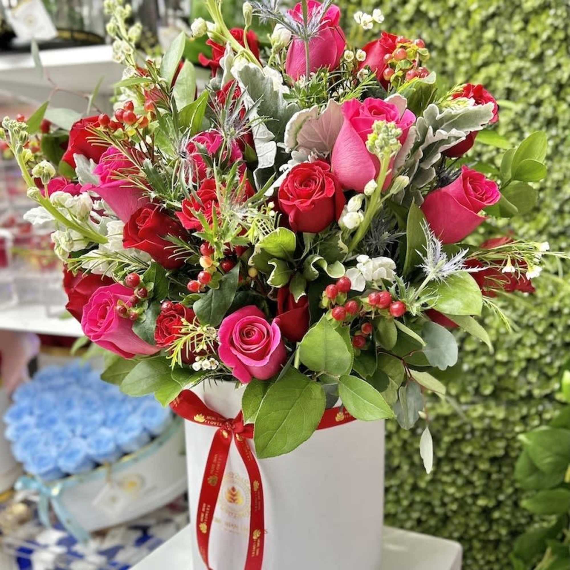Pink and red rose arrangement with berries in a white hatbox with a red ribbon.