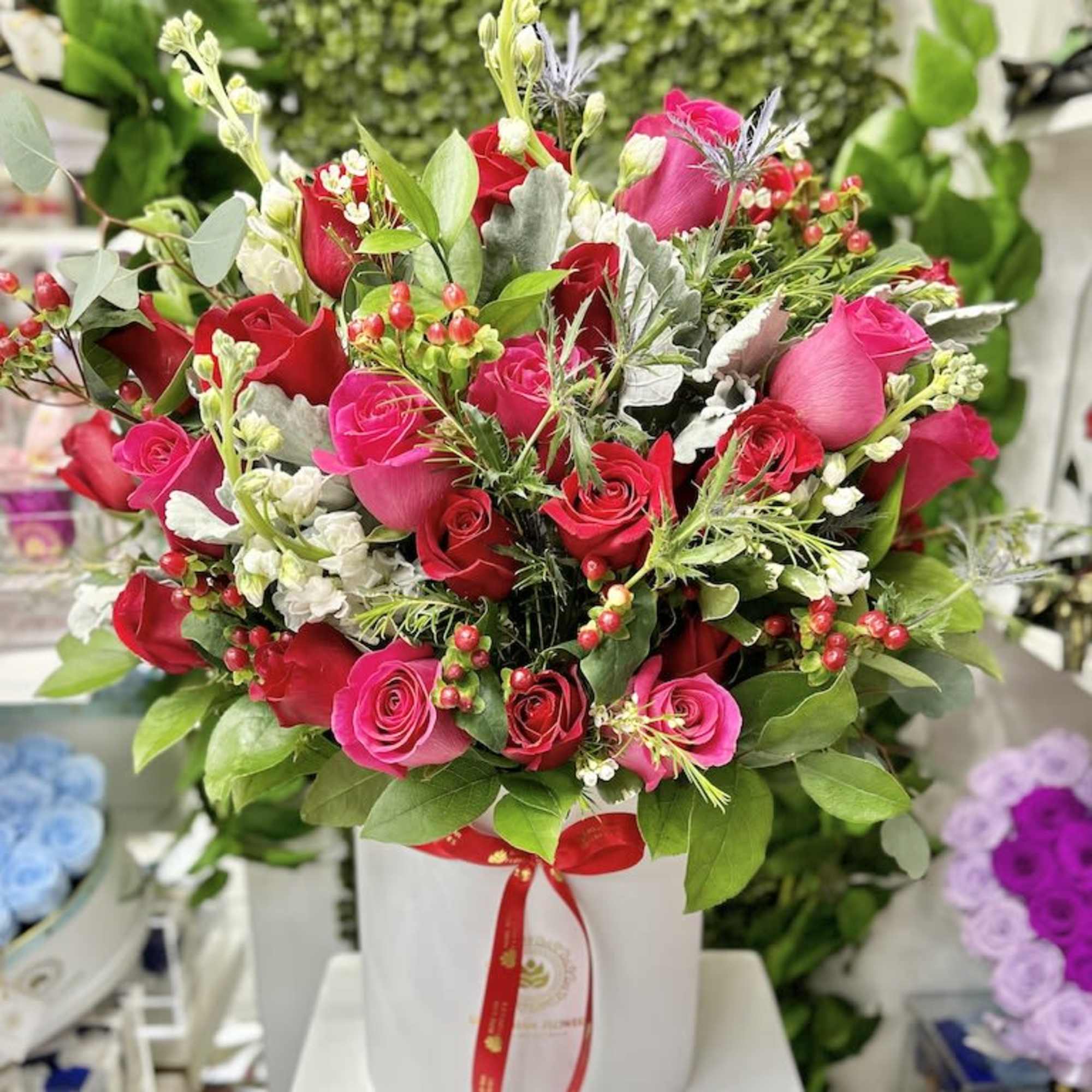 Large arrangement of red and hot pink roses in a white hatbox-style container with mixed filler flowers