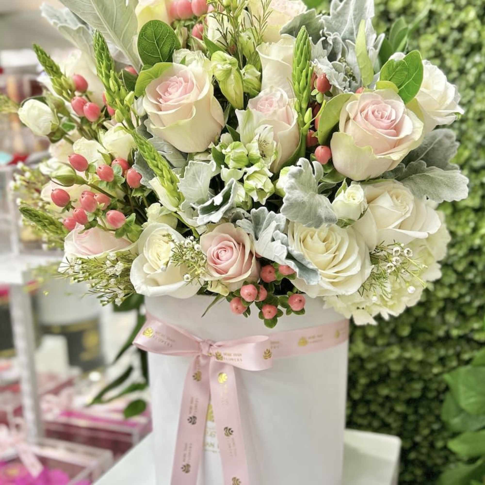 Hatbox arrangement of pale pink and white roses with pink berries in a white box tied with a pink ribbon