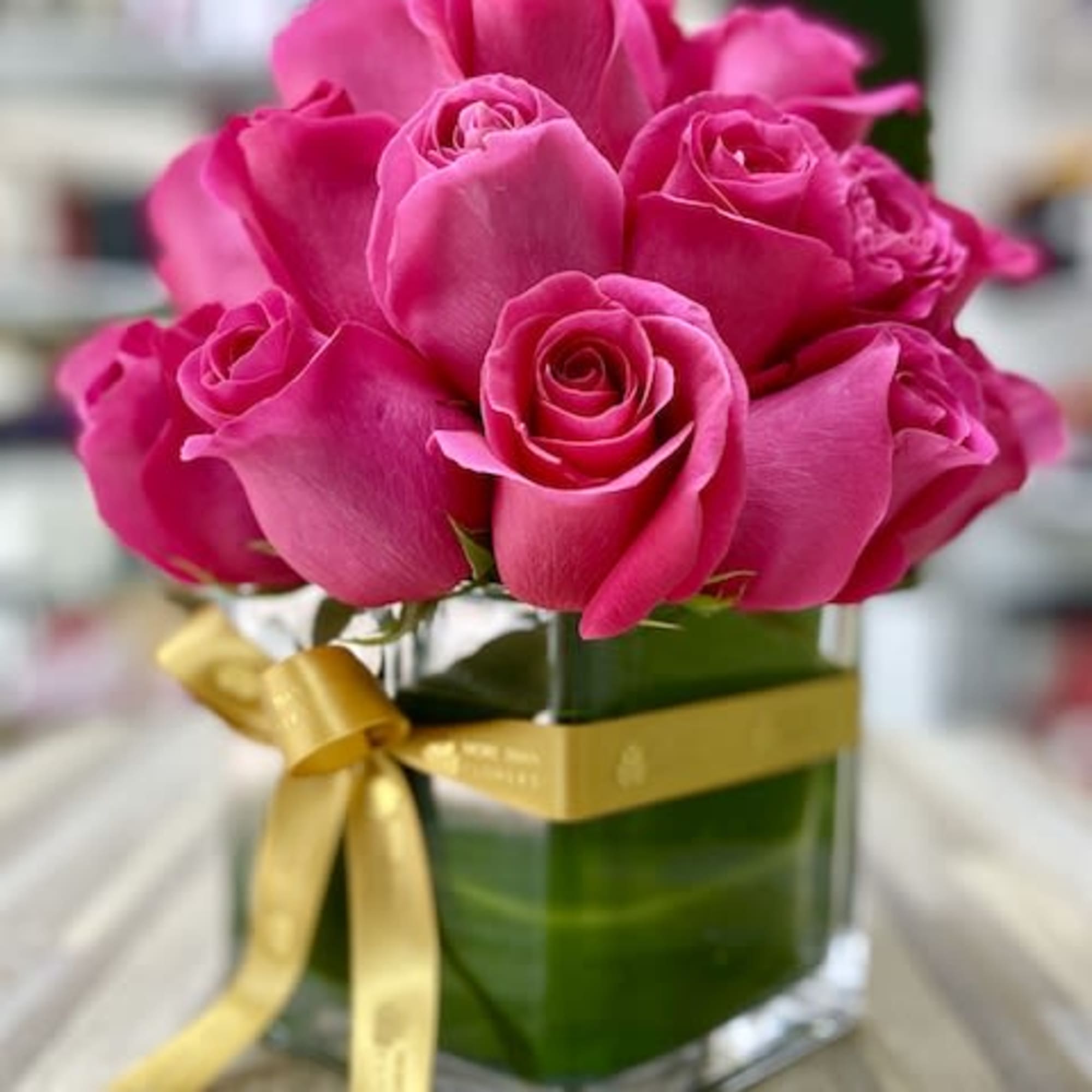 Hot pink roses arranged in a clear glass cube vase wrapped with a gold ribbon