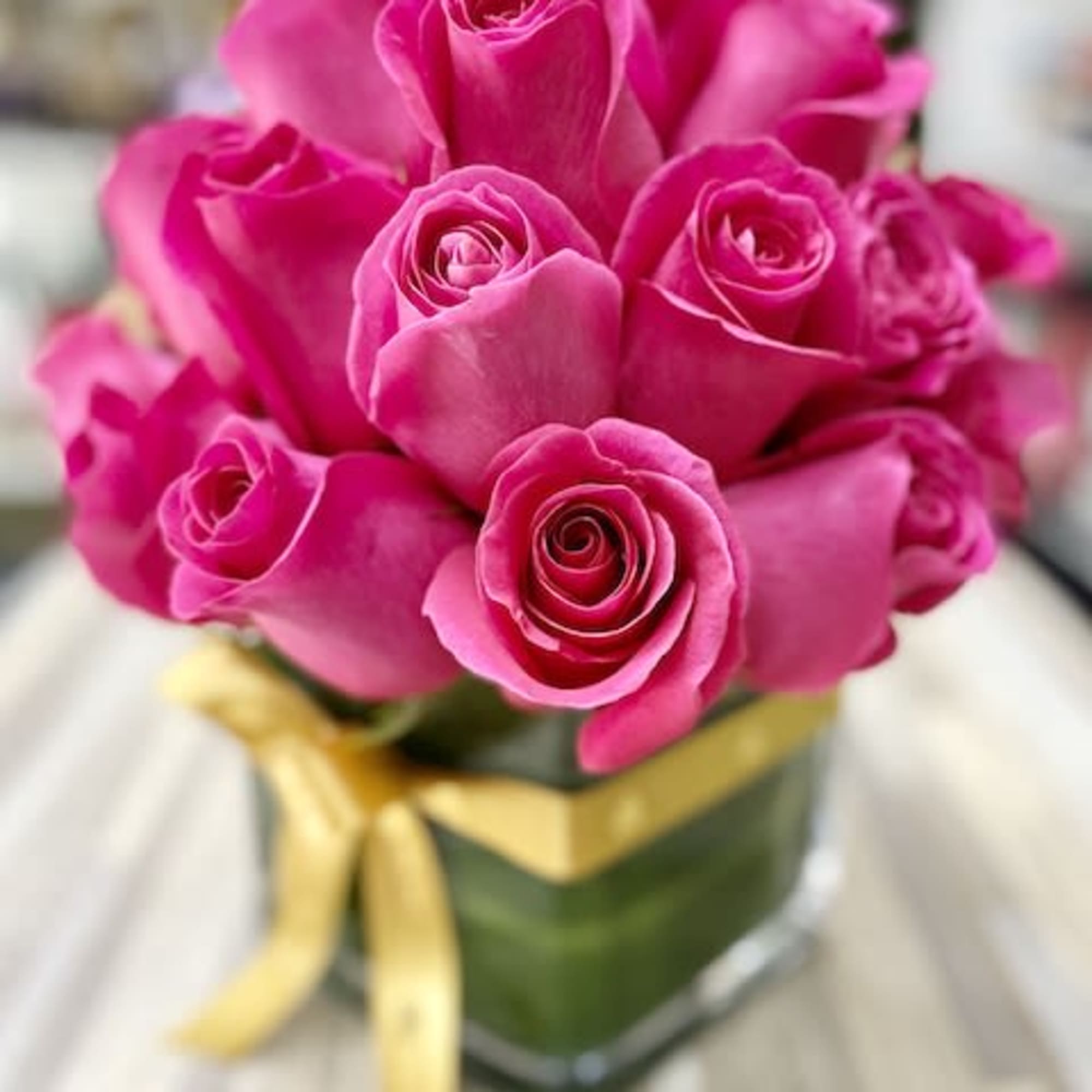 Compact arrangement of hot pink roses in a clear cube vase with a gold ribbon.