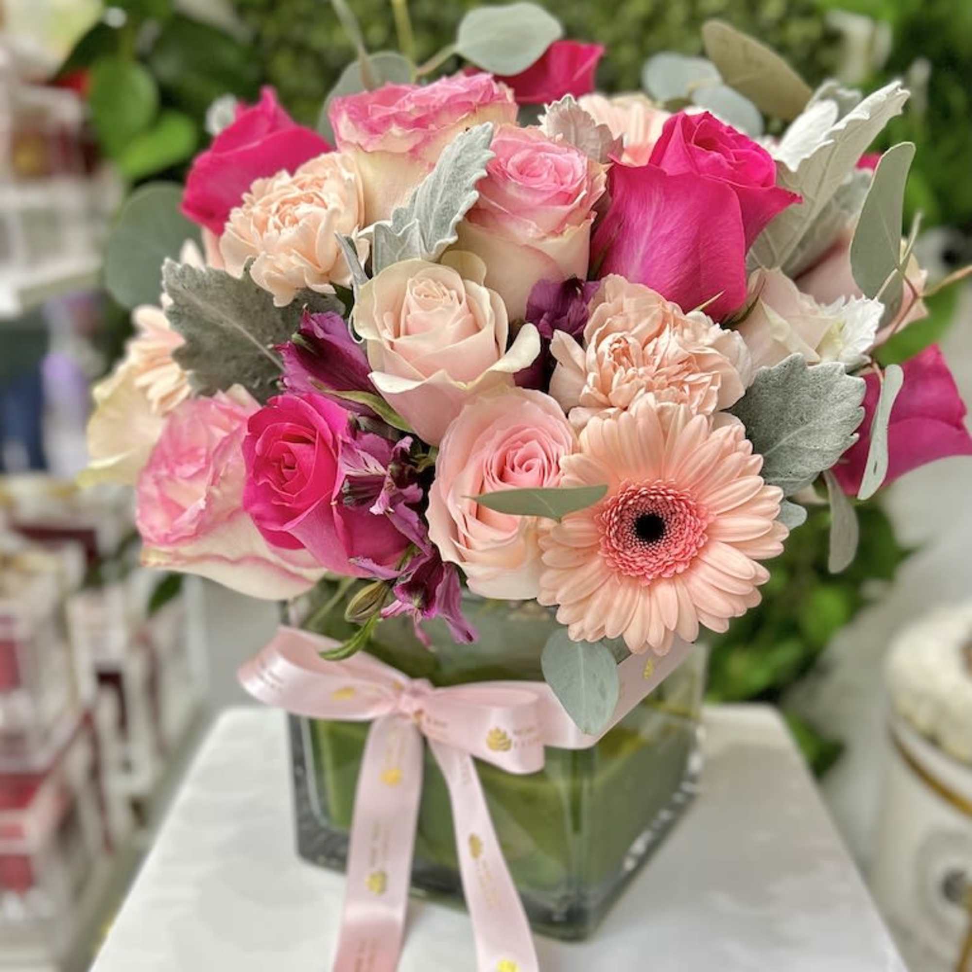 Pink and peach rose arrangement with gerbera daisies in a glass cube vase with pink ribbon