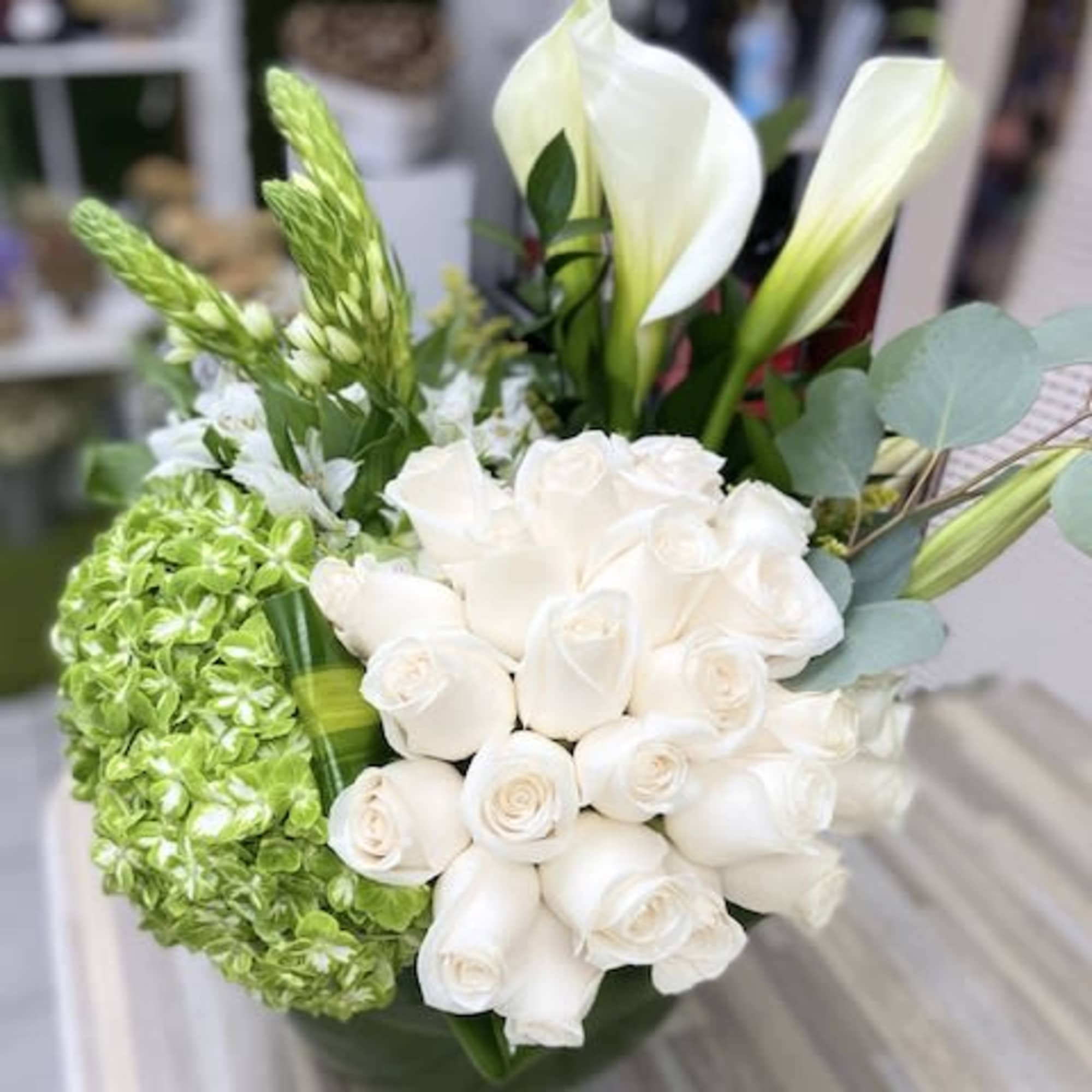 Compact arrangement of white roses, white calla lilies, and green hydrangea in a low glass vase.