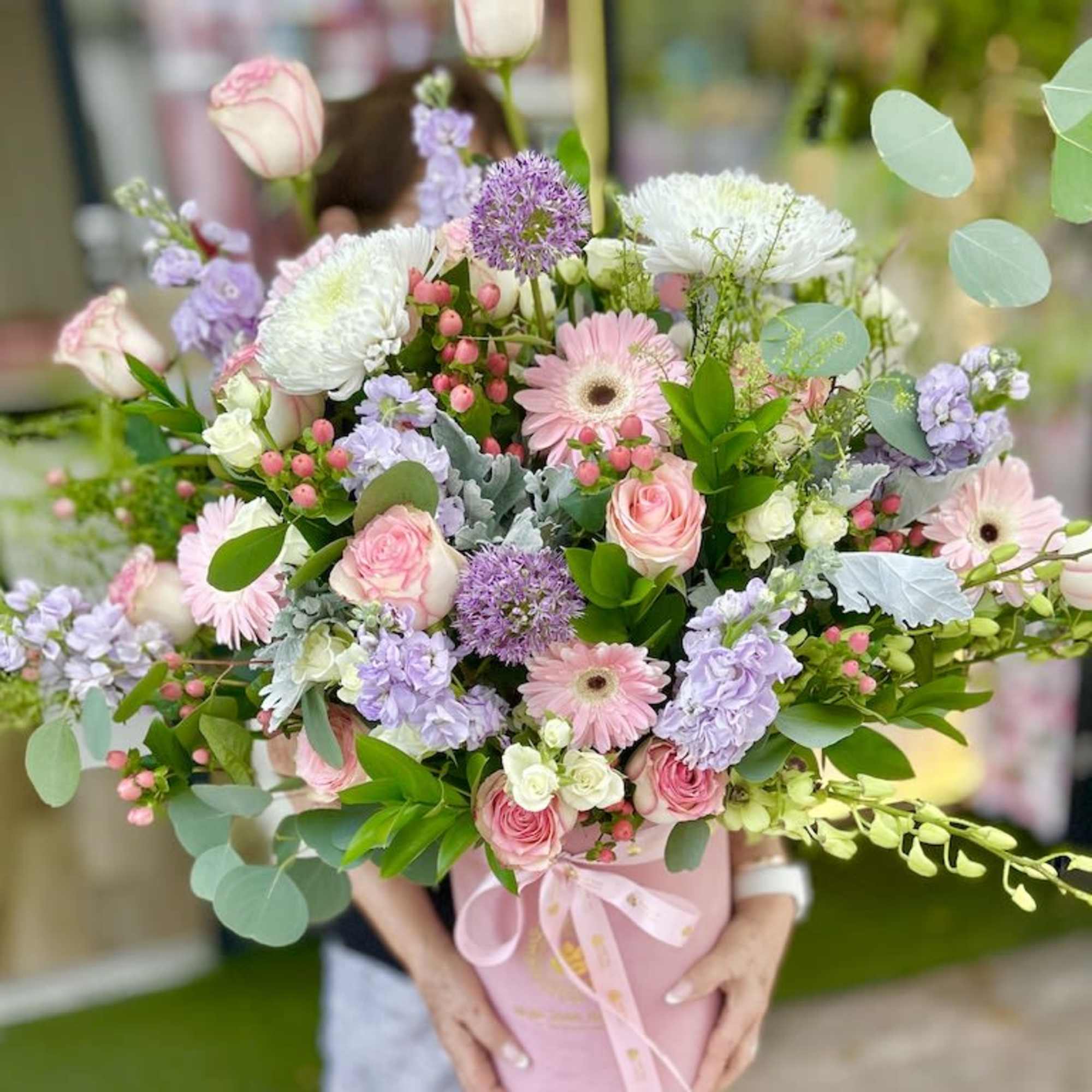 Large pastel arrangement of pink roses and gerberas with lavender blooms in a pink hatbox-style container