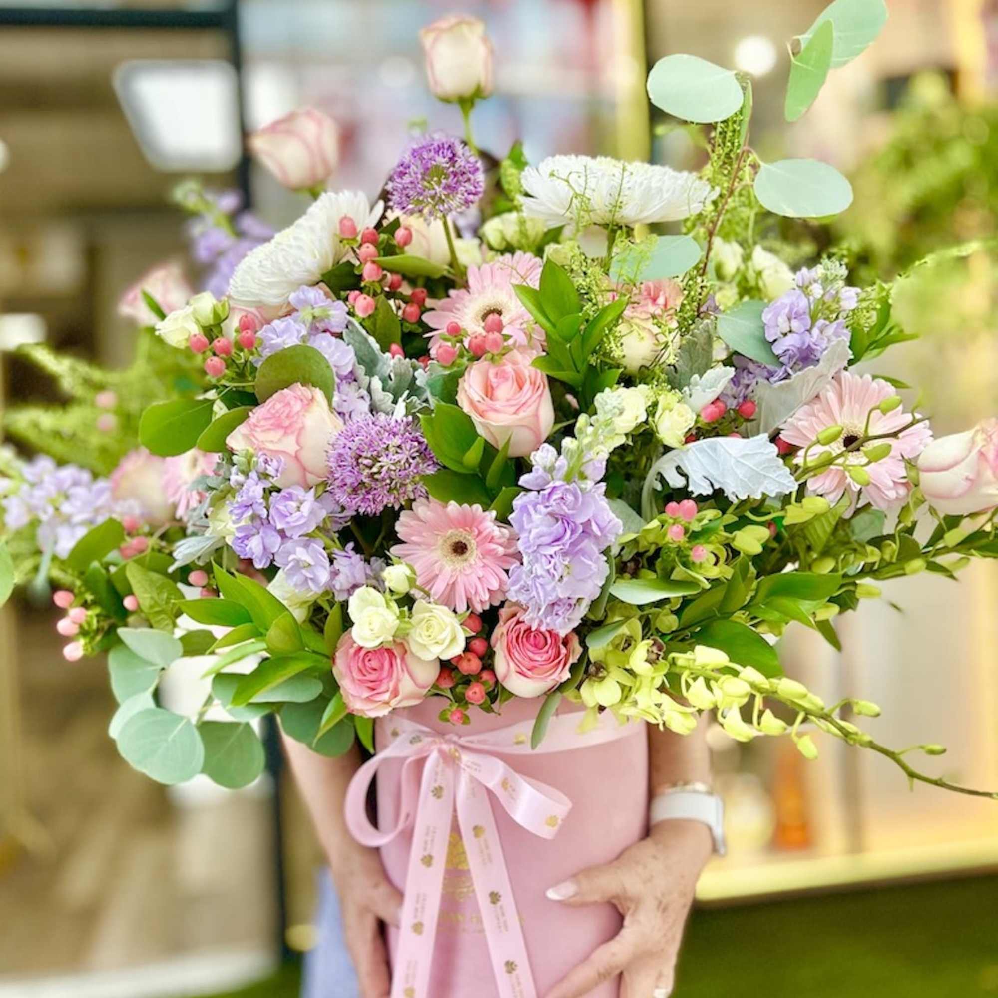 Large pastel flower arrangement with pink roses, gerberas, and lavender blooms in a pink hatbox with ribbon.