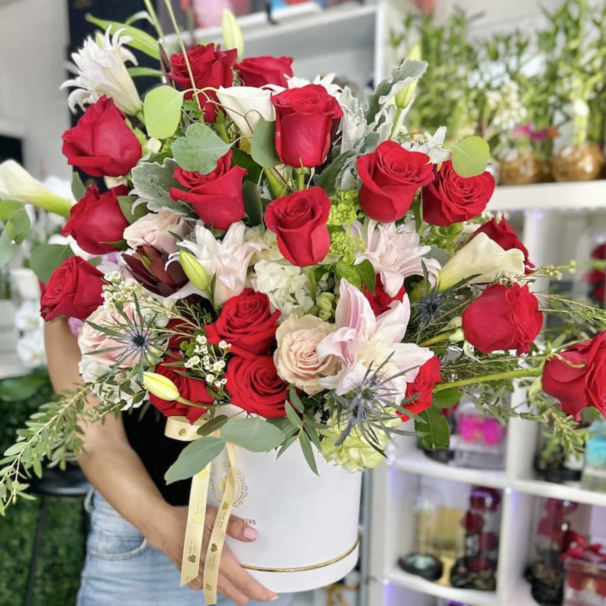 Large arrangement of red roses with pale pink and white lilies in a round white hatbox container