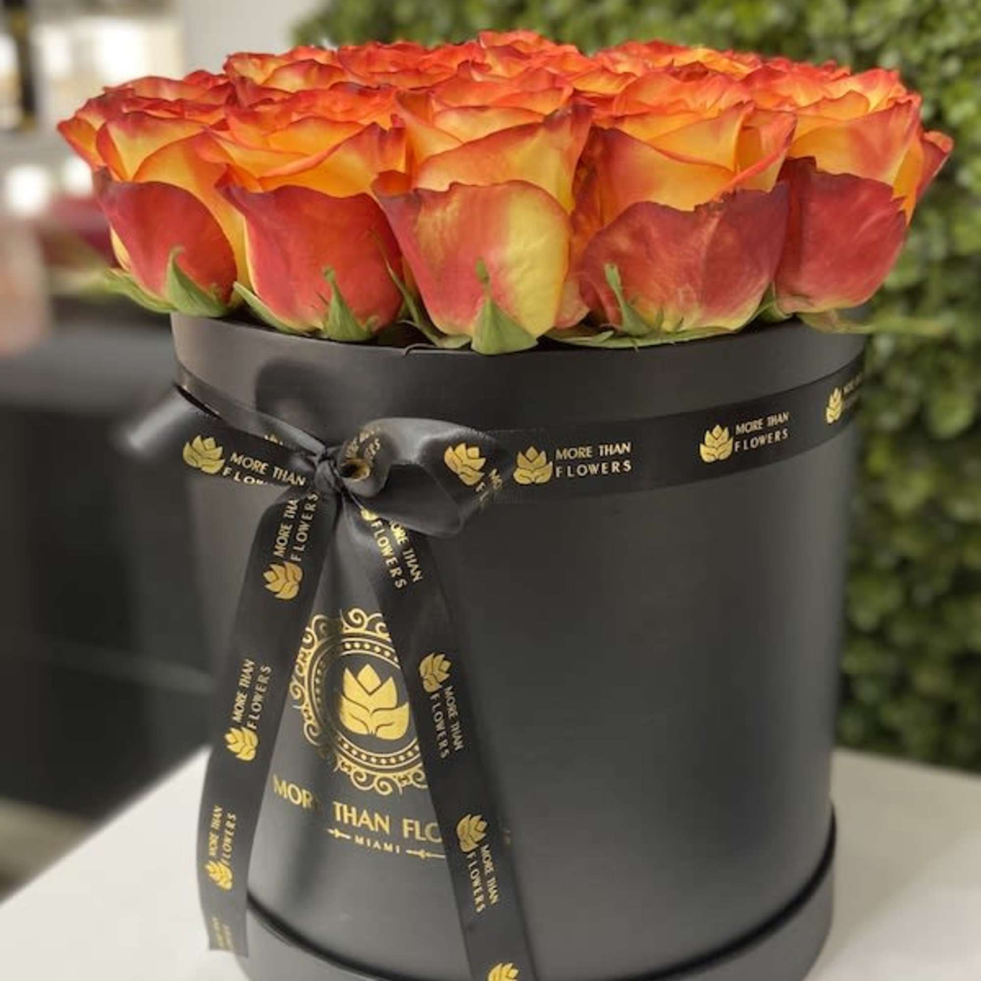 Round black hatbox filled with orange and yellow roses and tied with a black ribbon.