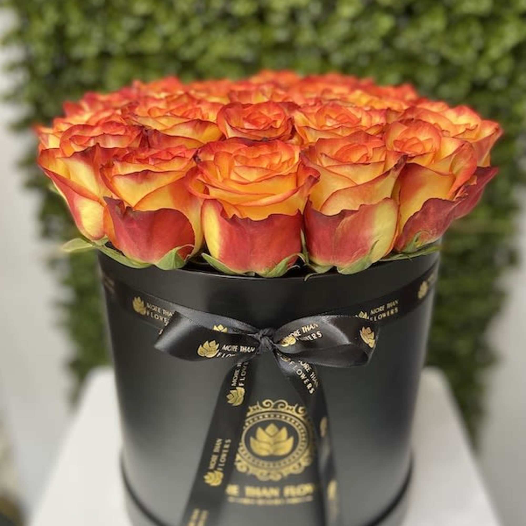 Round black hatbox filled with orange and yellow roses tied with a black ribbon.