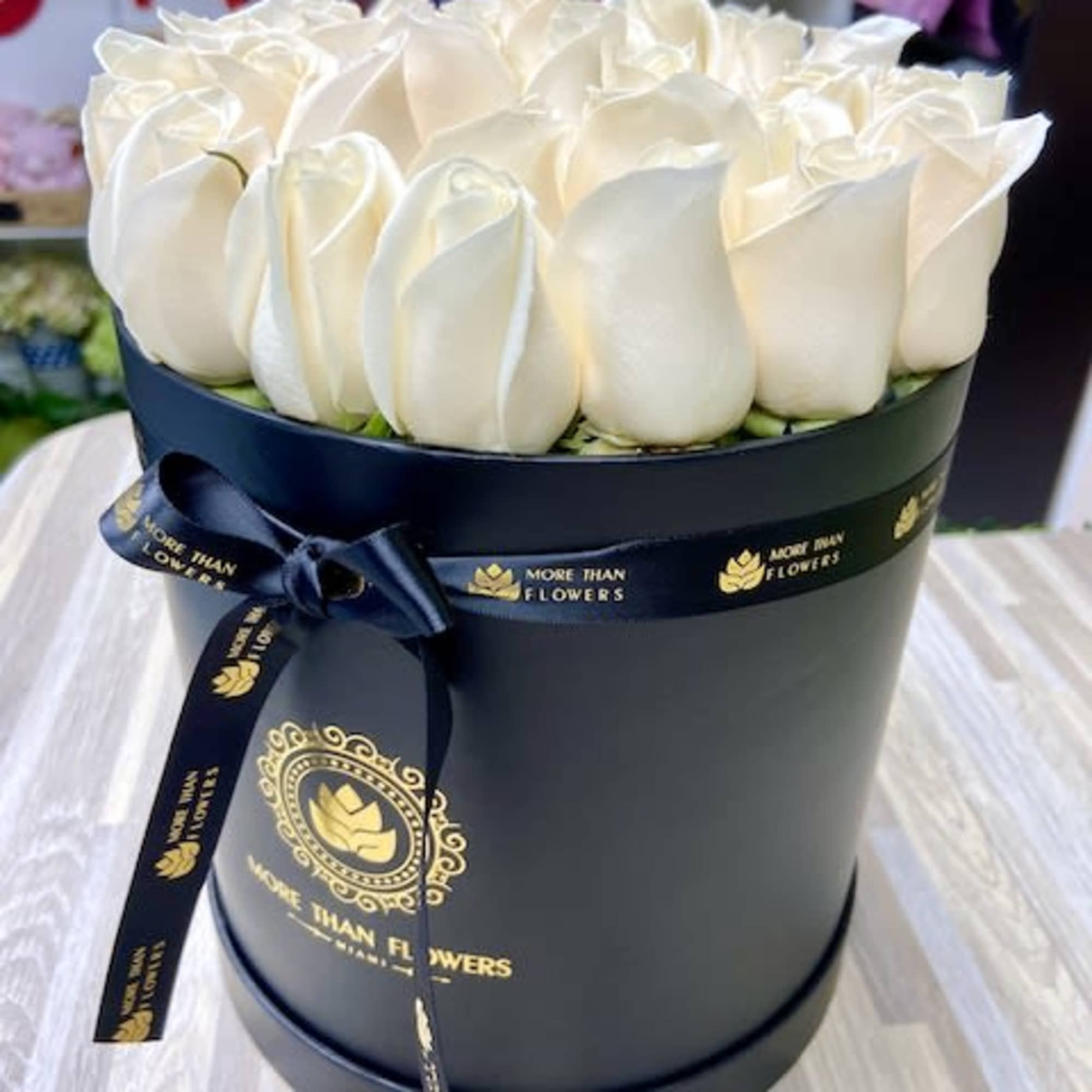 Round black hatbox filled with tightly packed white roses and a black ribbon bow.