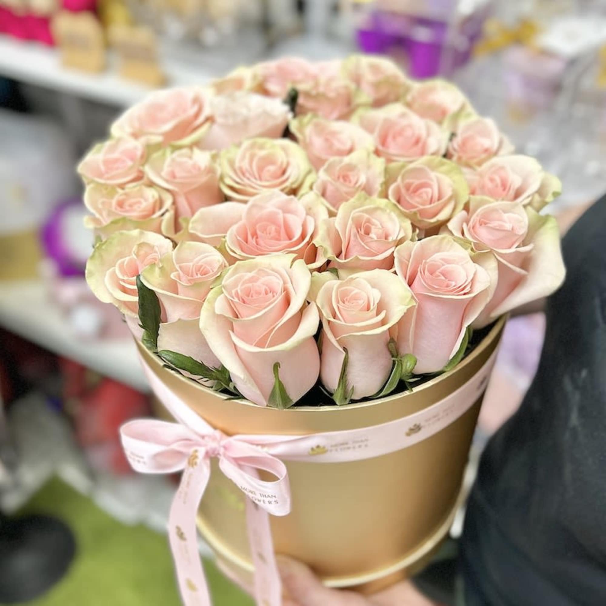 Round gold hat box filled with tightly packed pale pink roses and tied with a pink ribbon.