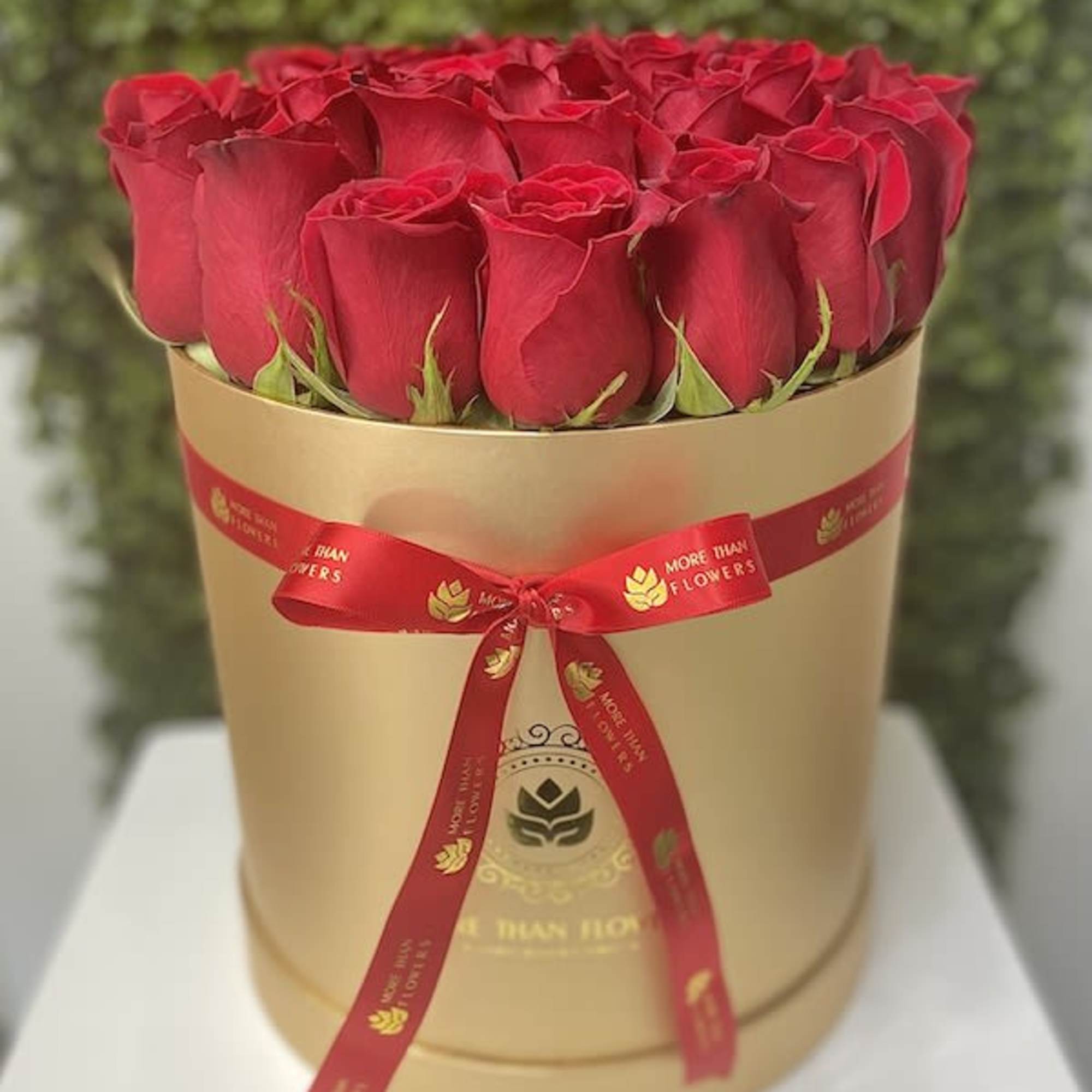 Round box of tightly packed red roses in a gold hatbox with a red ribbon bow
