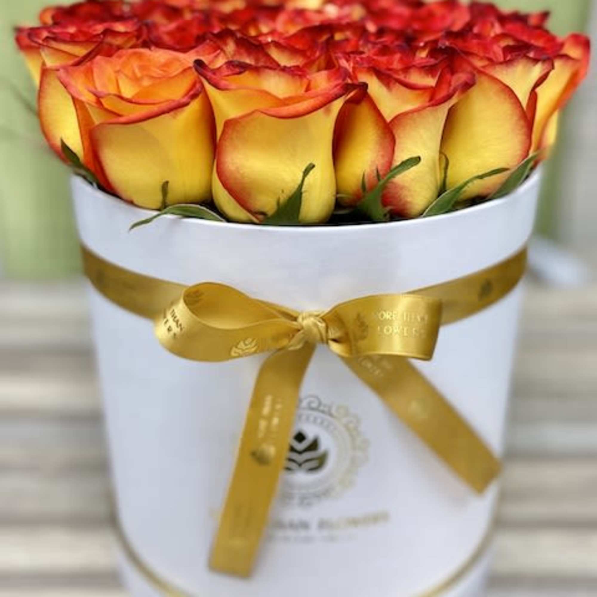 Round hatbox filled with yellow roses edged in red, tied with a gold ribbon