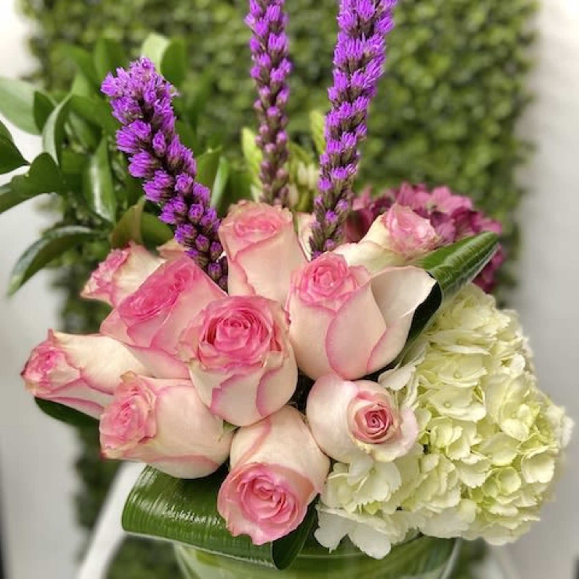 Pink roses and white hydrangea with tall purple flower spikes in a green glass vase