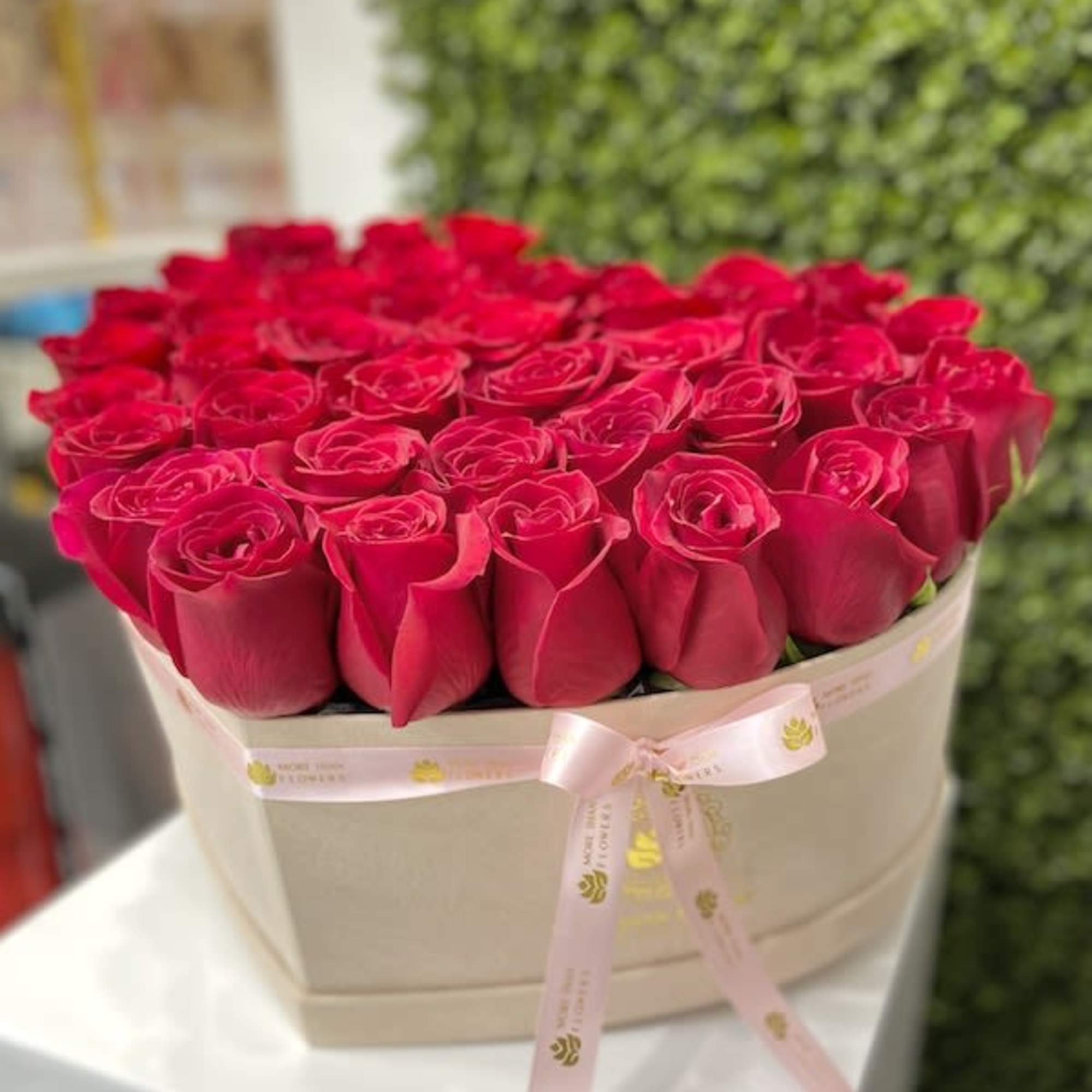 Box of red roses arranged tightly in a beige hat box with a pink ribbon bow