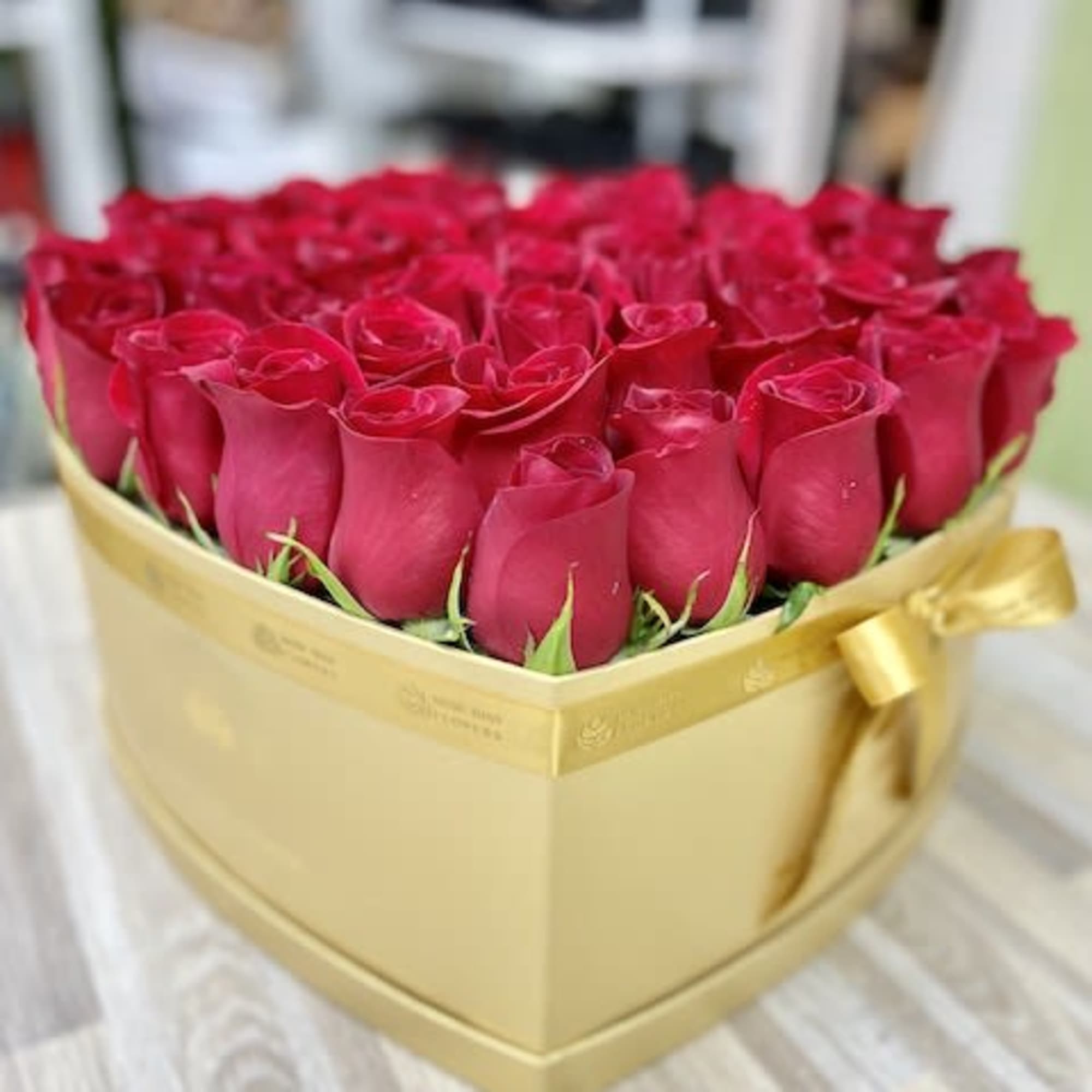 Heart-shaped gold box filled with tightly packed red roses.