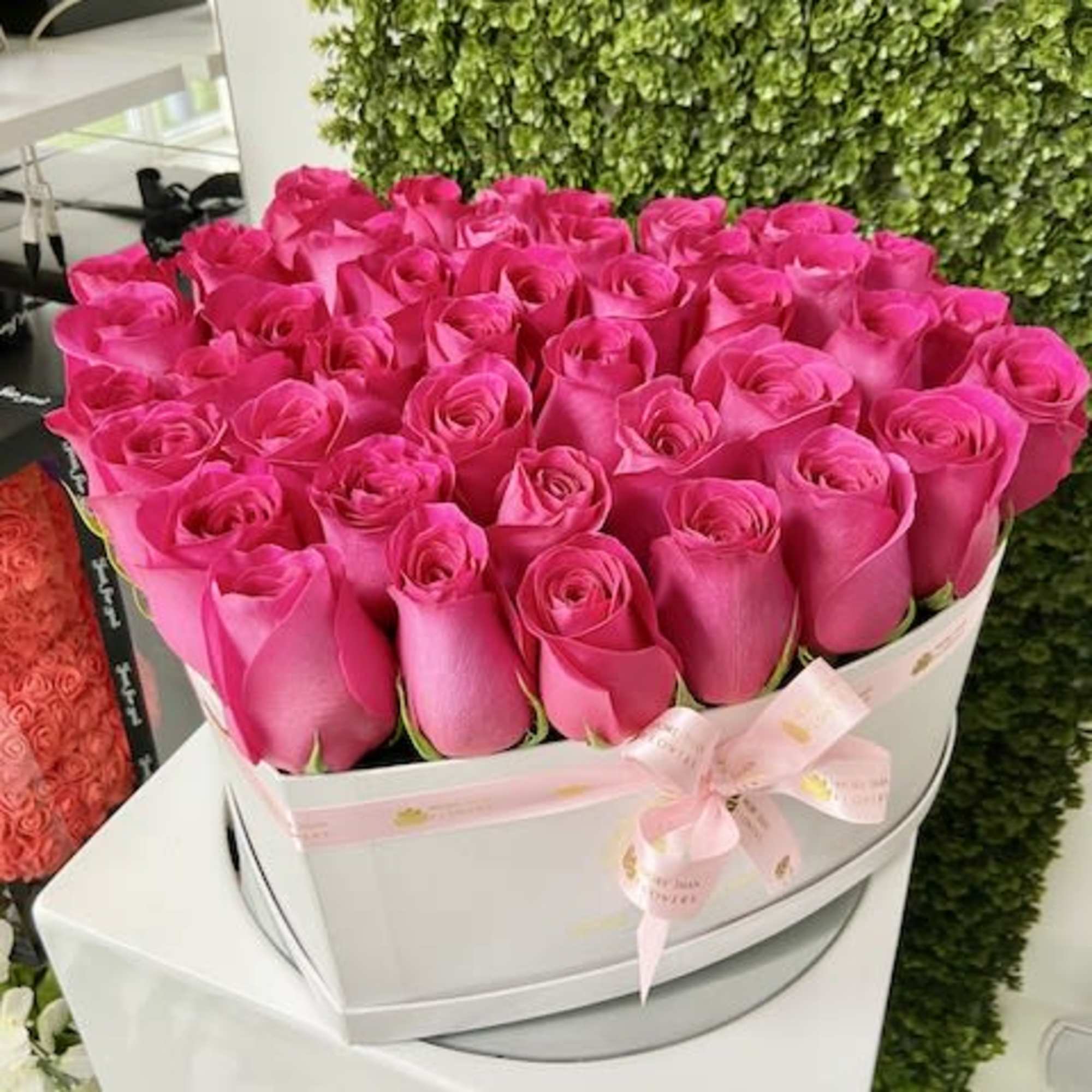 Round white hatbox filled with tightly packed bright pink roses and a pink ribbon bow