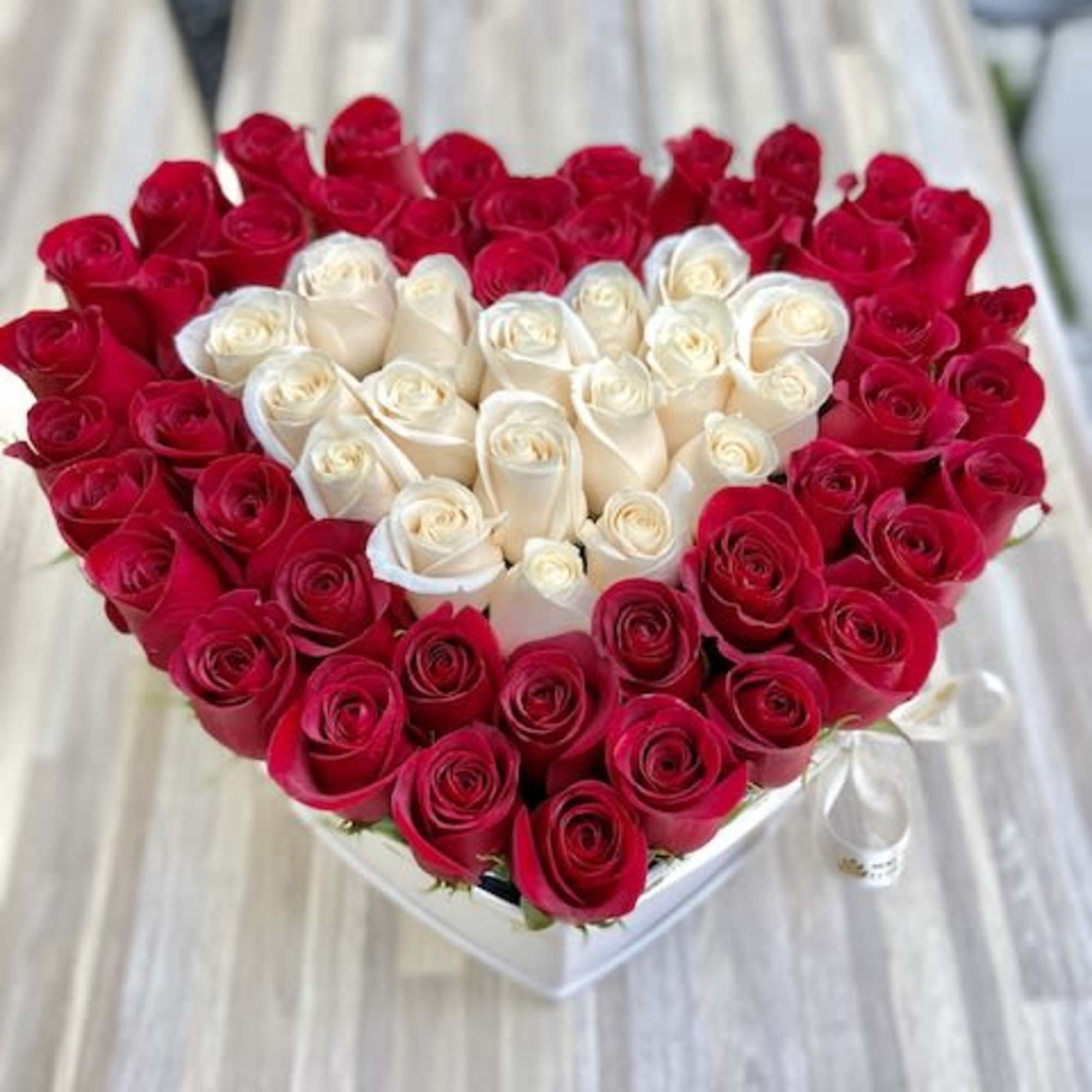 Heart-shaped arrangement of red and white roses in a white box.