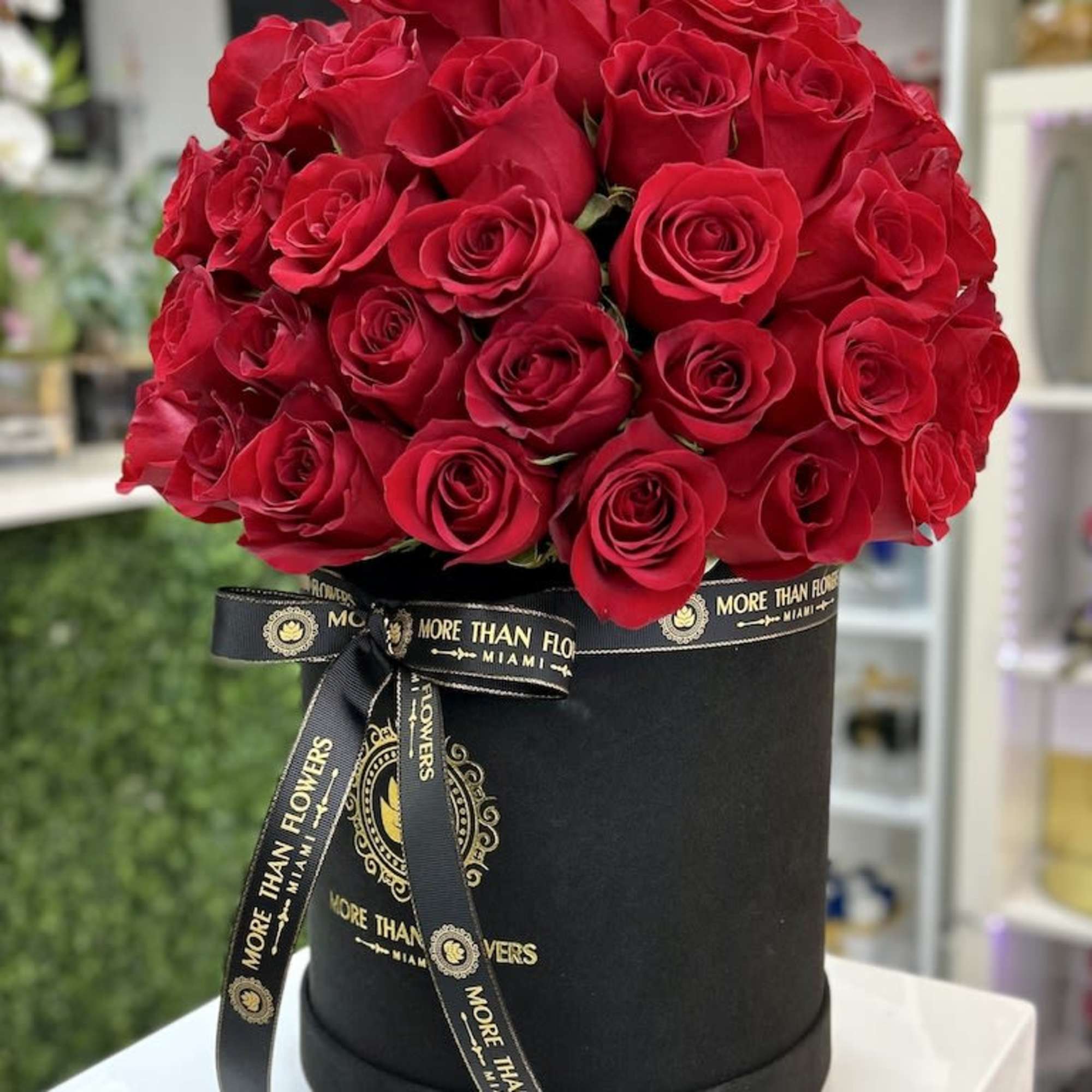 Round black hatbox filled with a dense dome of red roses and tied with a branded black ribbon