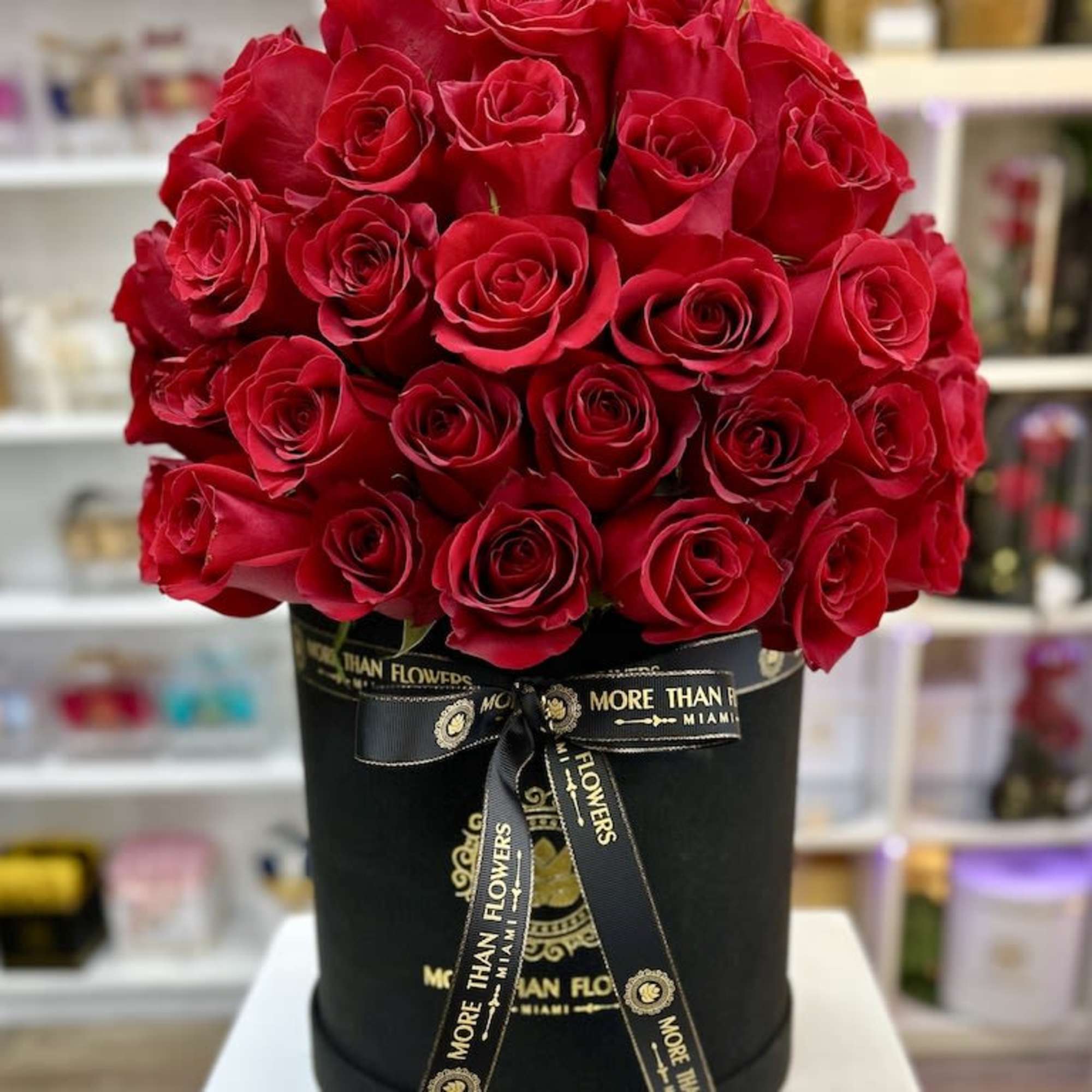 Large dome of red roses arranged in a black hatbox with branded ribbon on a white tabletop